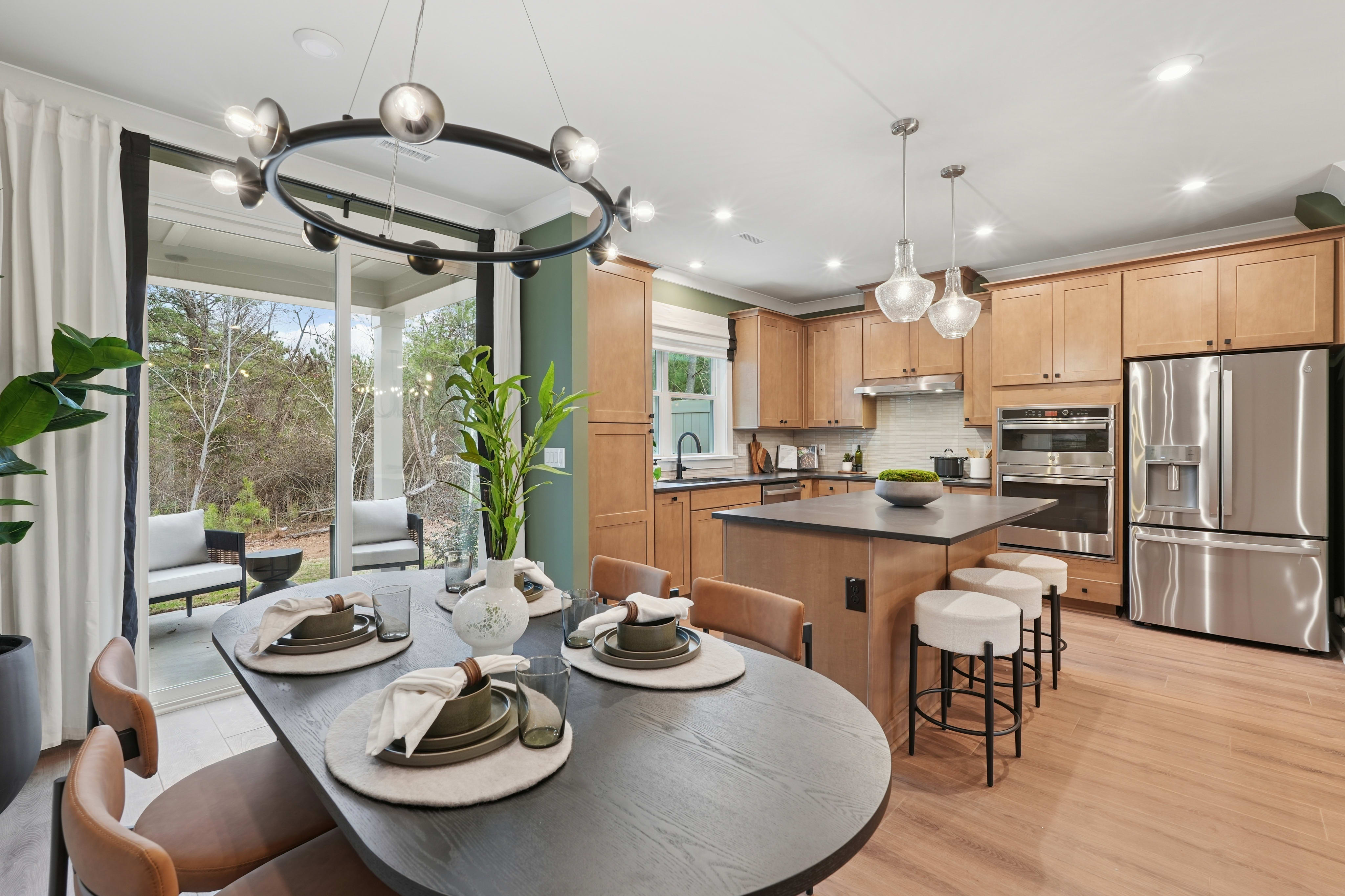 A modern and well-appointed kitchen with a round dining table, pendant lighting, and large windows overlooking a natural outdoor setting.