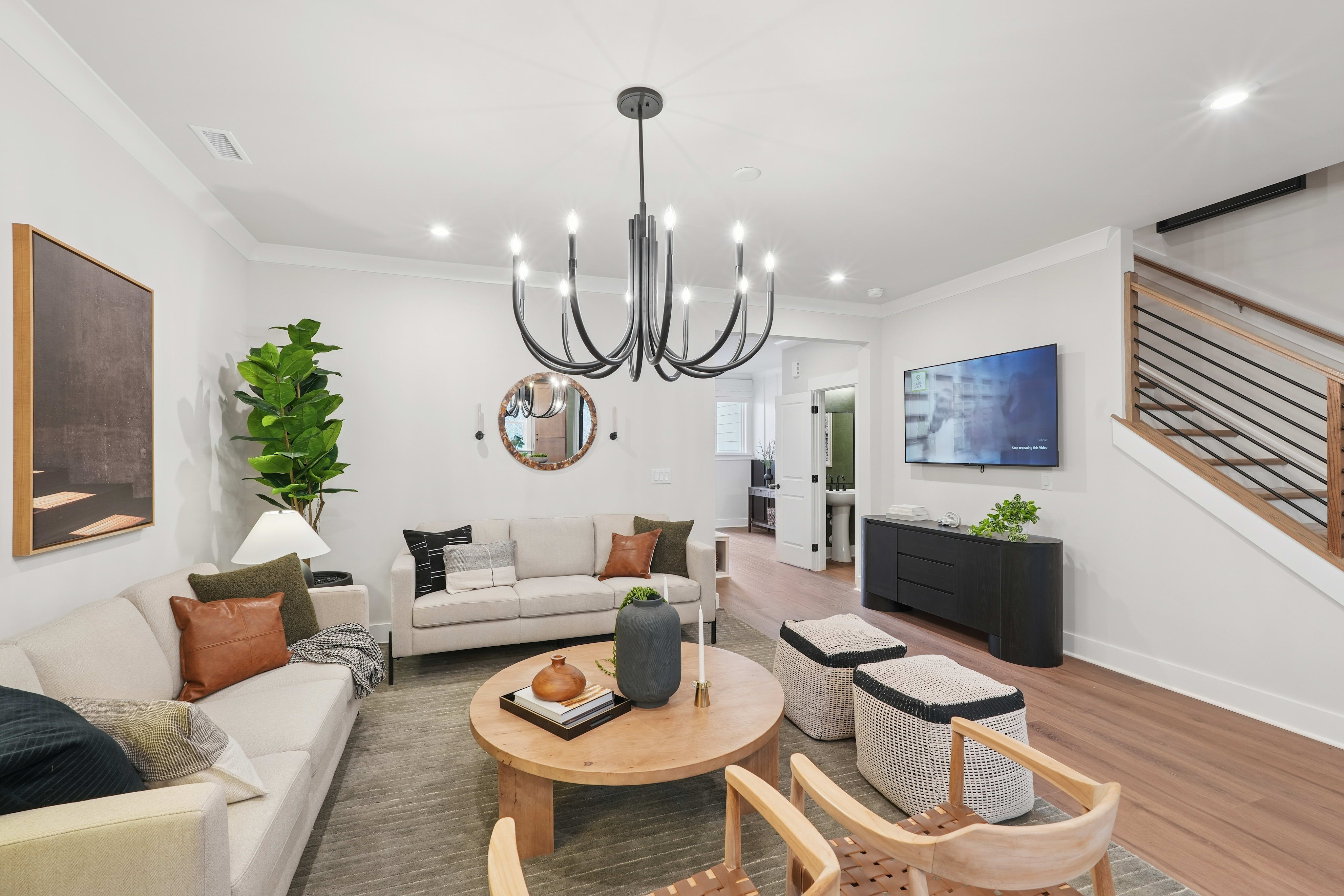 A modern and stylish living room with a large chandelier, comfortable sofas, and various decorative elements such as plants, artwork, and a wooden coffee table.
