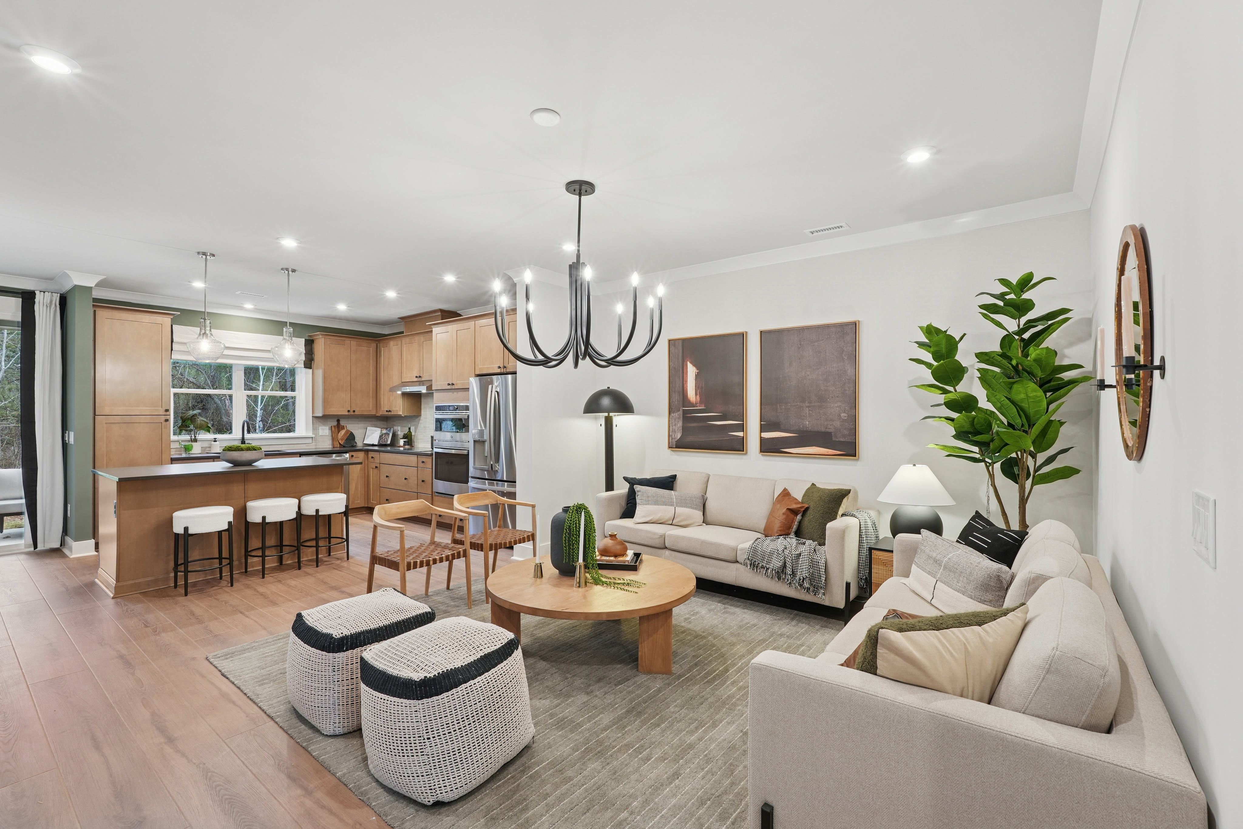 A modern and cozy open-concept living room and kitchen area with wooden floors, neutral-toned furniture, and various decorative elements such as plants and artwork.