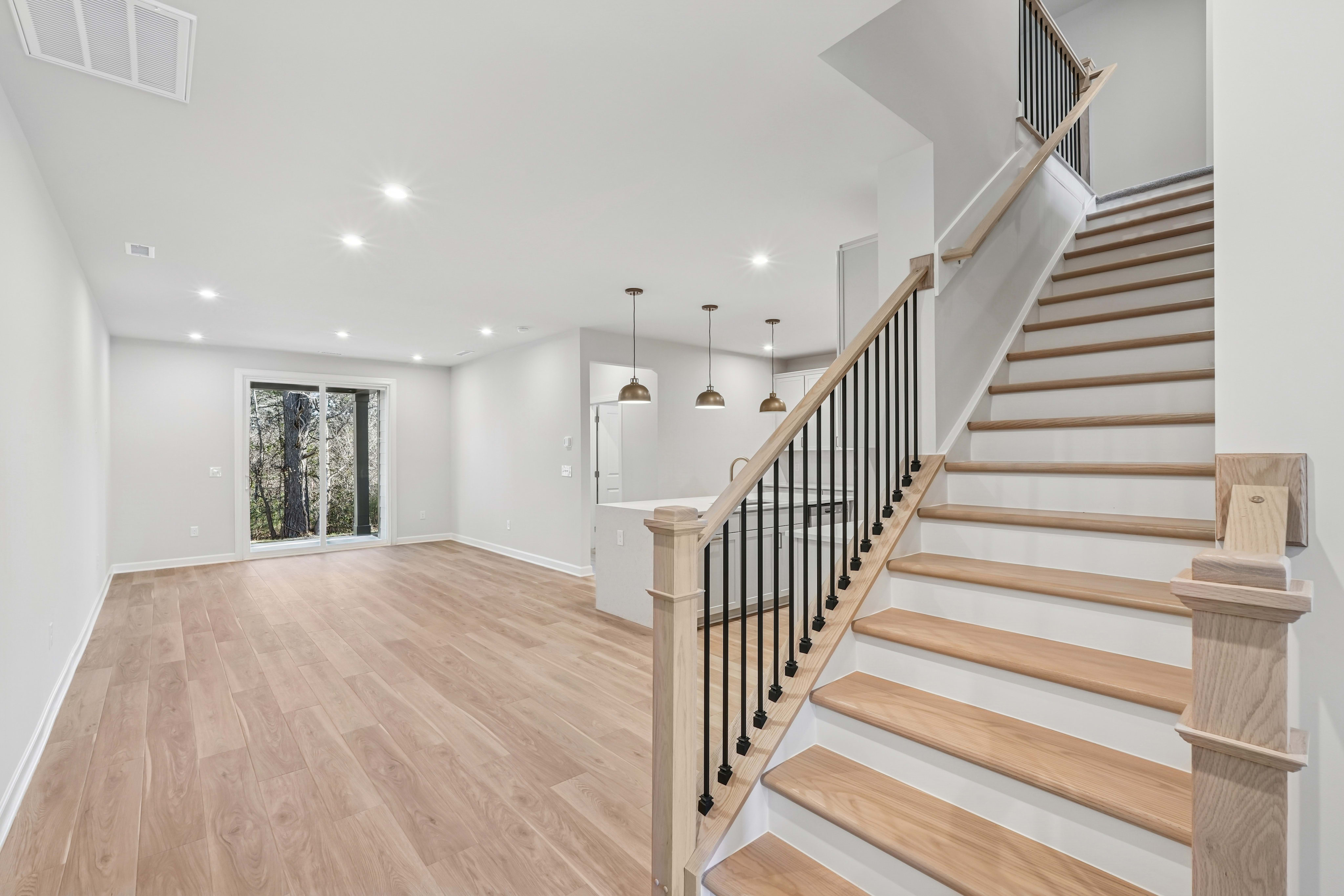 A spacious and modern entryway with a wooden staircase, hardwood floors, and pendant lighting fixtures, leading to a bright and open living space.