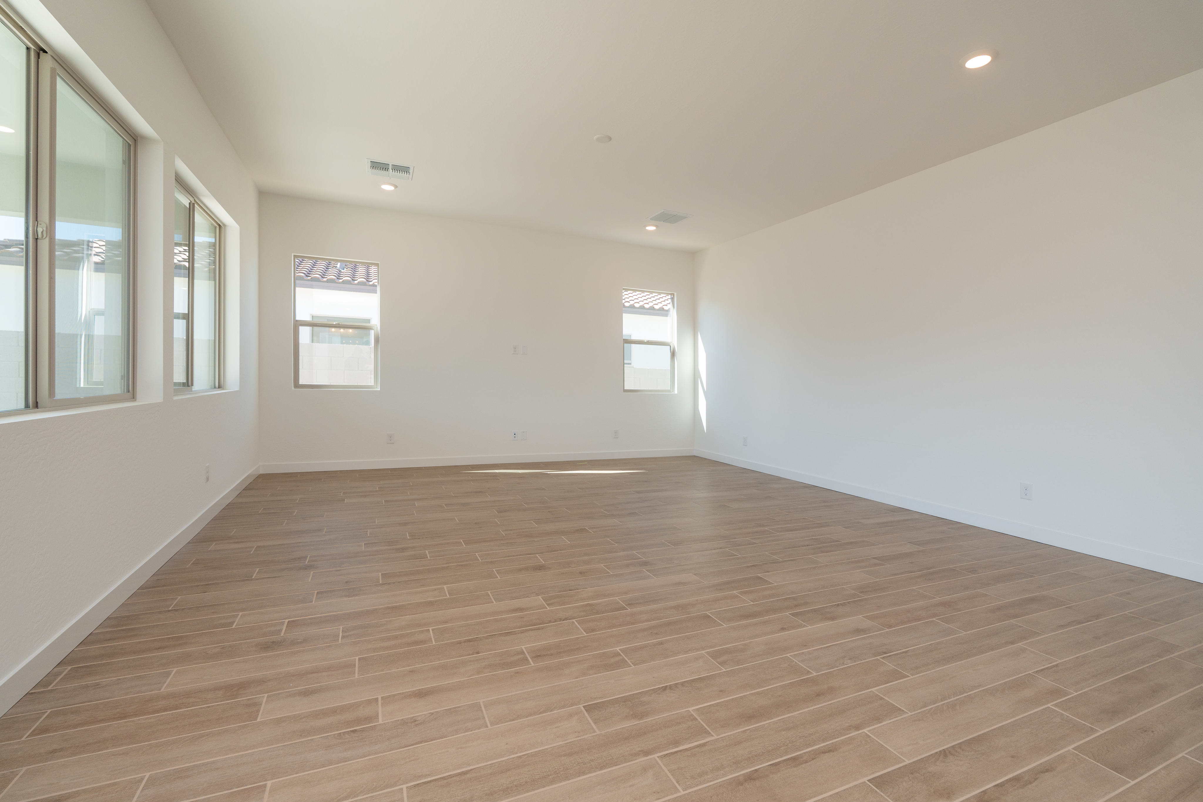 An empty room with white walls and a hardwood floor, featuring large windows that allow natural light to fill the space.