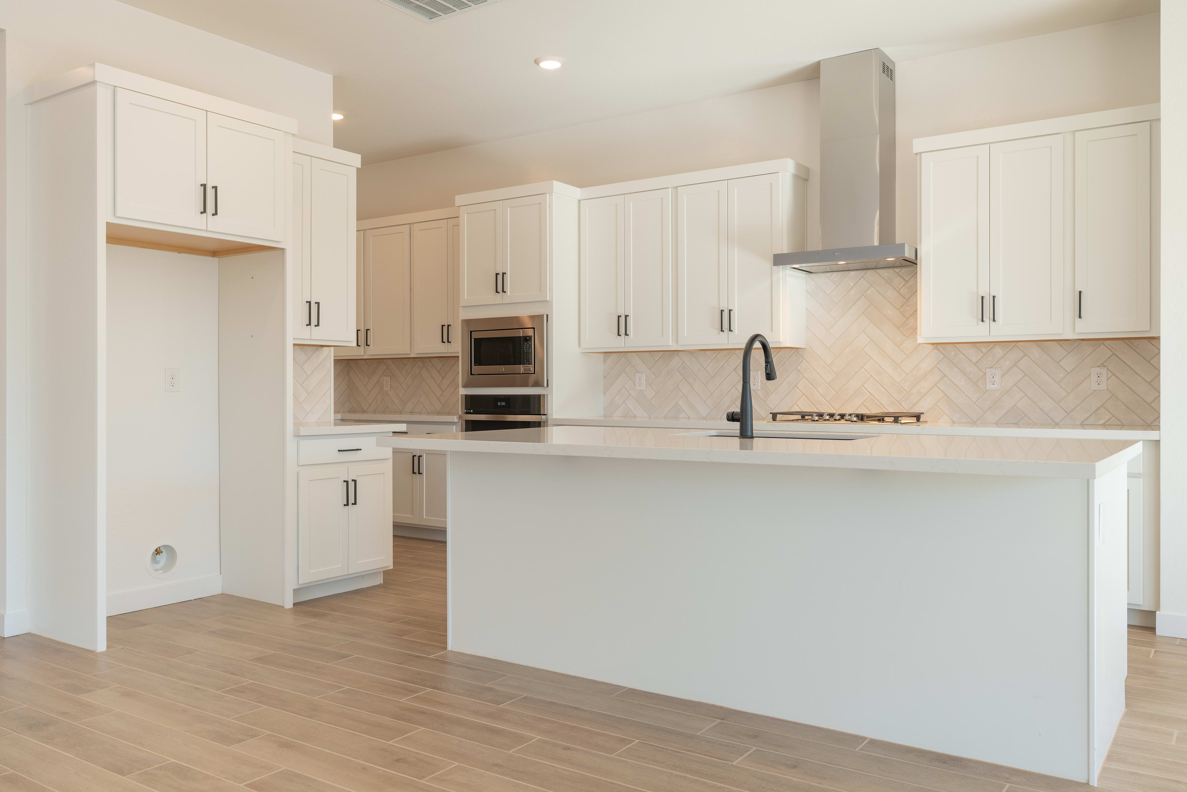 A modern, bright kitchen with white cabinets, a central island, and hardwood floors.