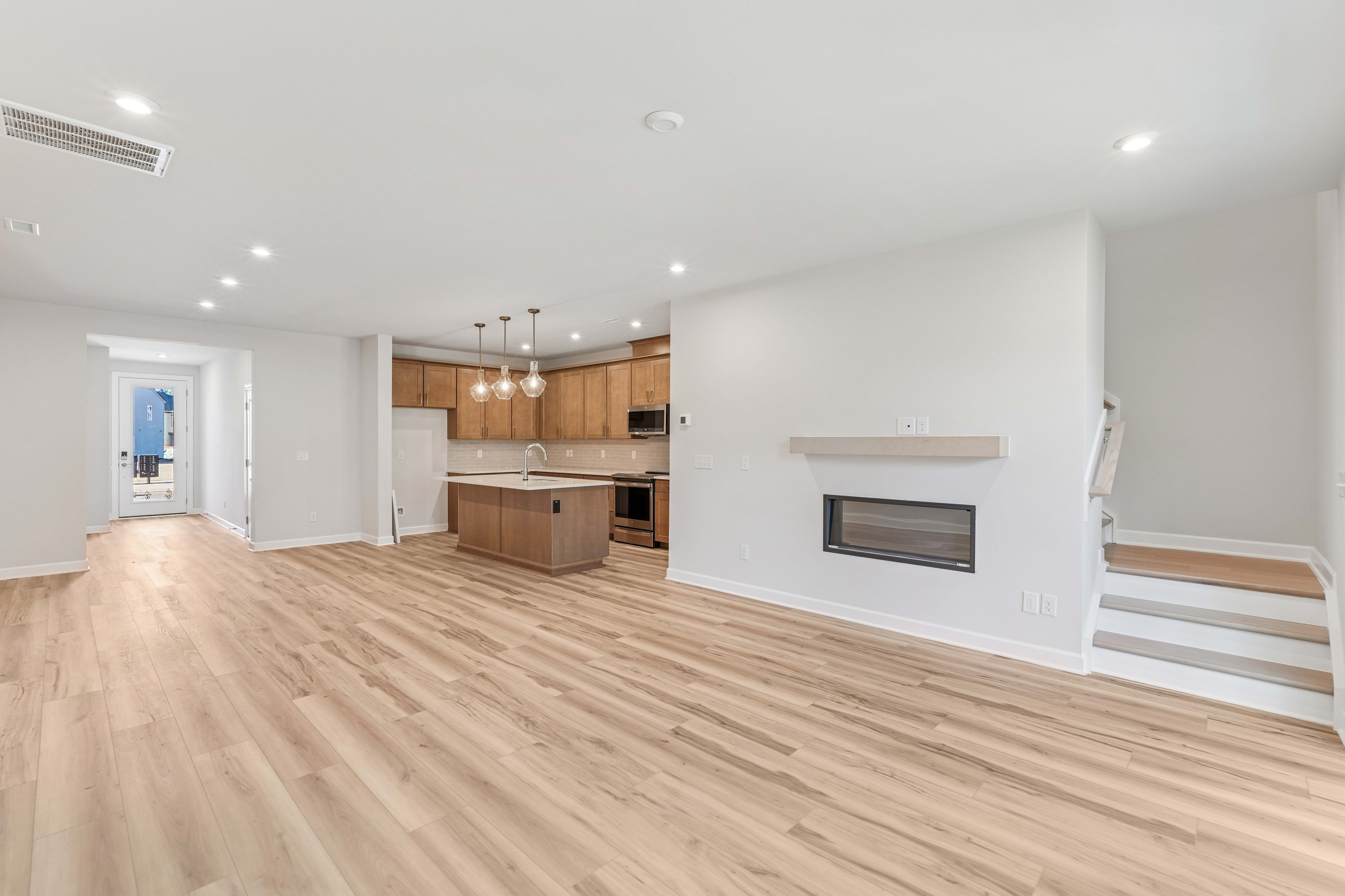 A spacious and modern open-plan living area with a kitchen, hardwood floors, and a fireplace in the background.