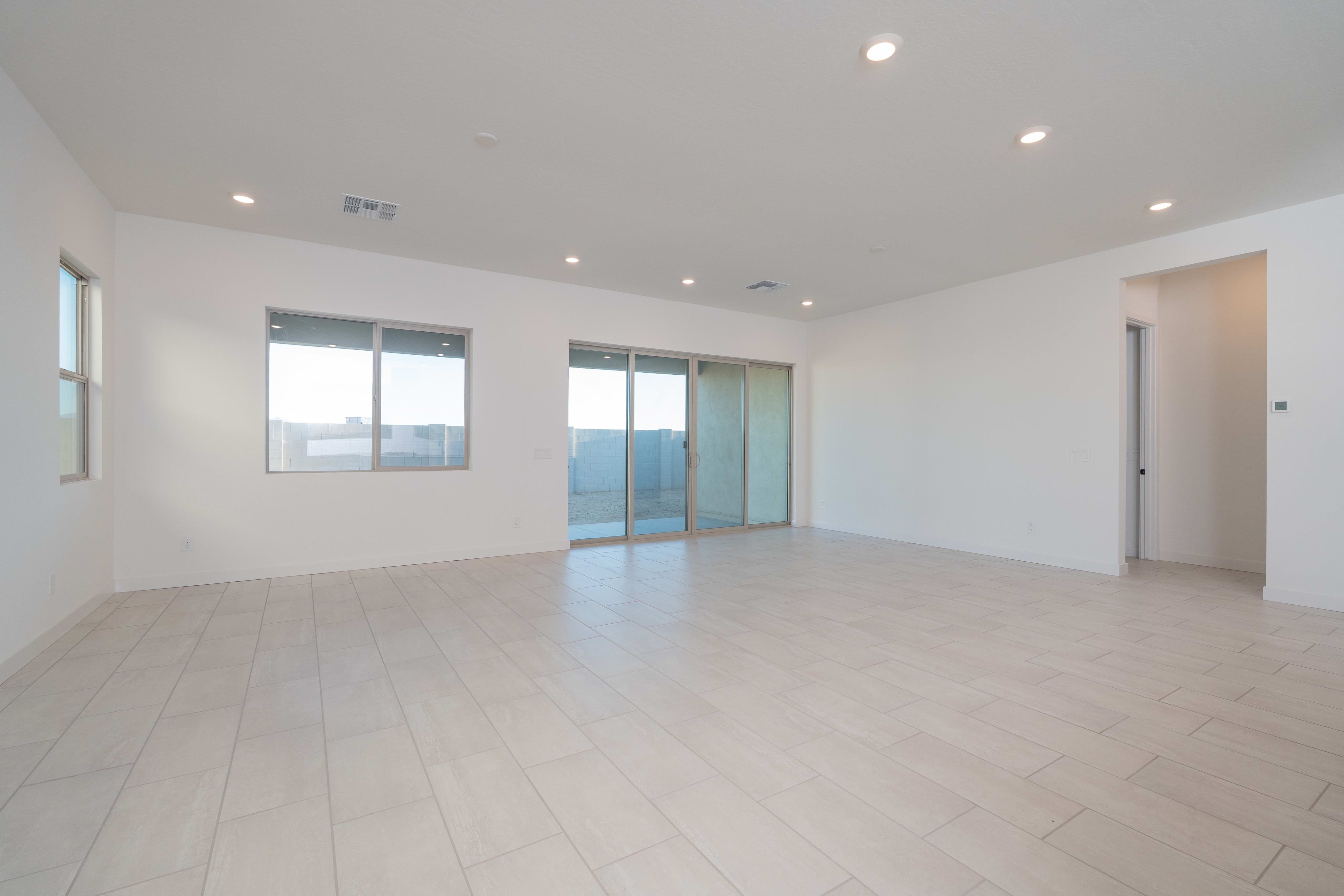 A spacious, well-lit room with large windows, a smooth white floor, and a sliding glass door leading to an outdoor area.