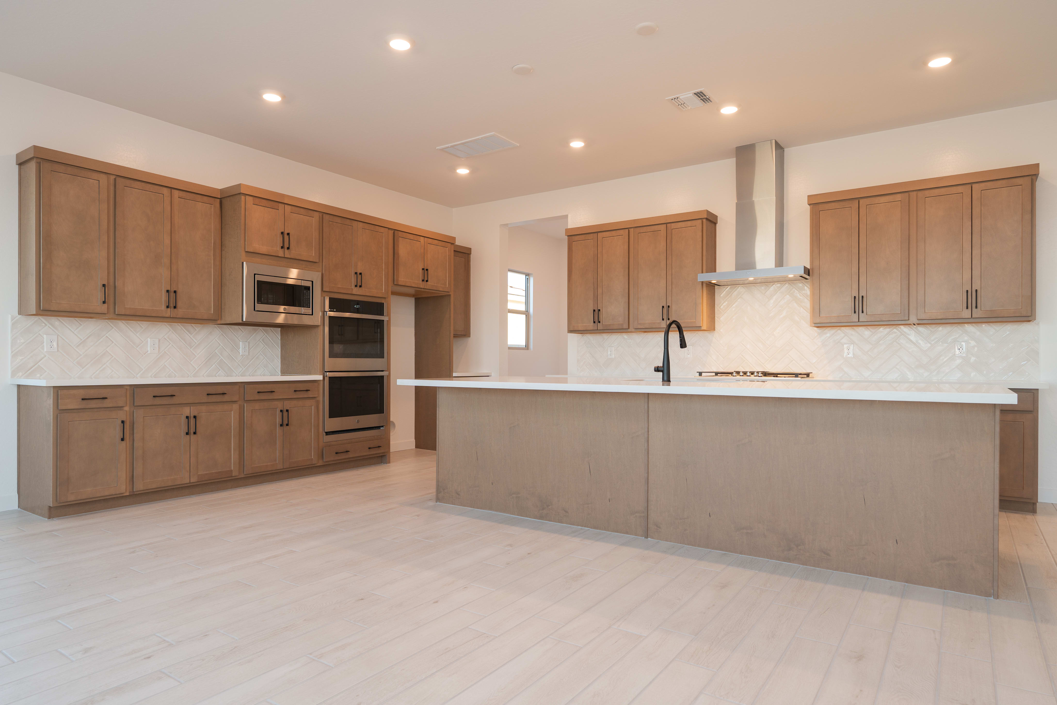 A modern, open-concept kitchen with light wood cabinets, a white countertop, and a tiled backsplash, set against a bright and airy background.