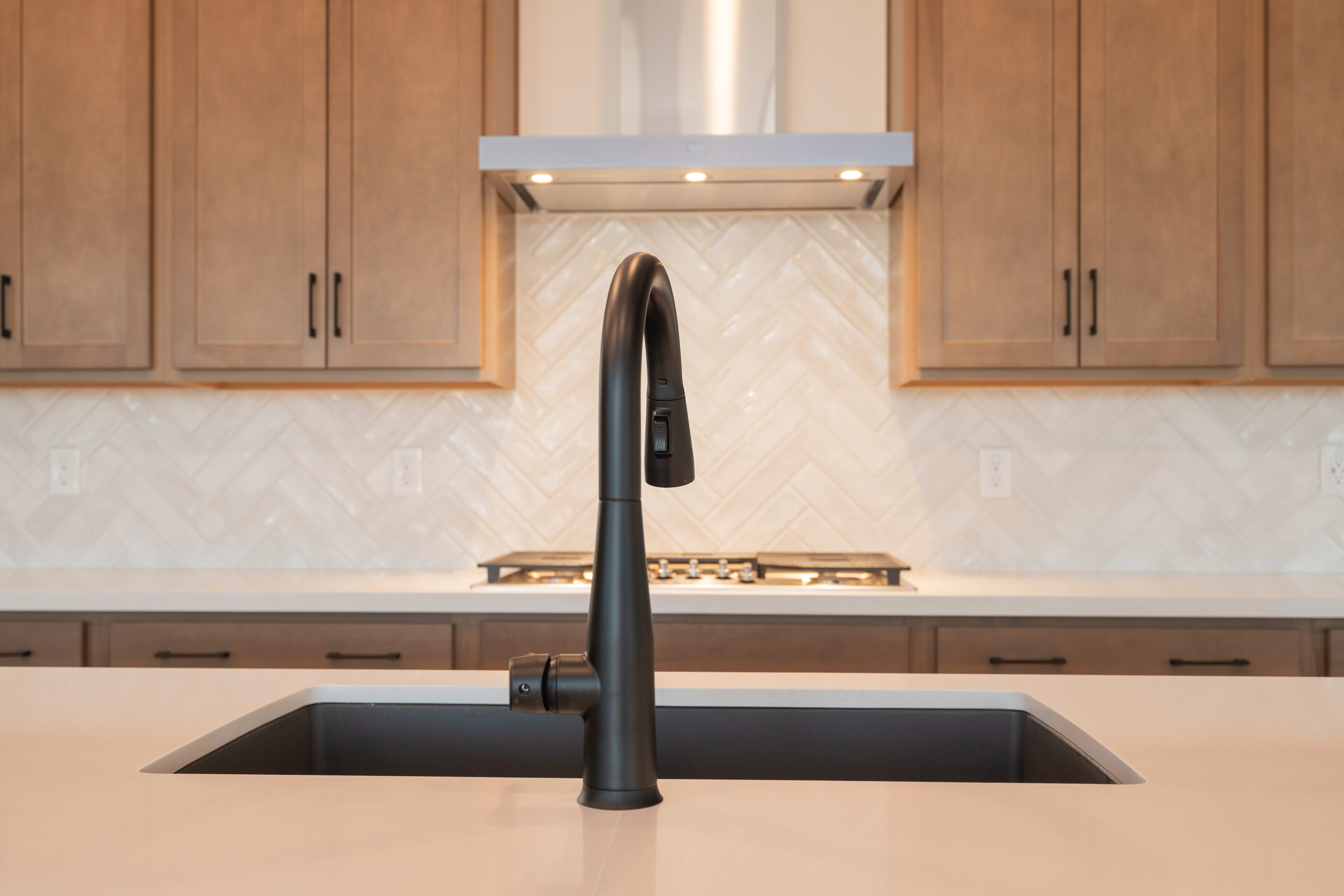A modern kitchen with wooden cabinets, a black sink faucet, and a backsplash in the background.