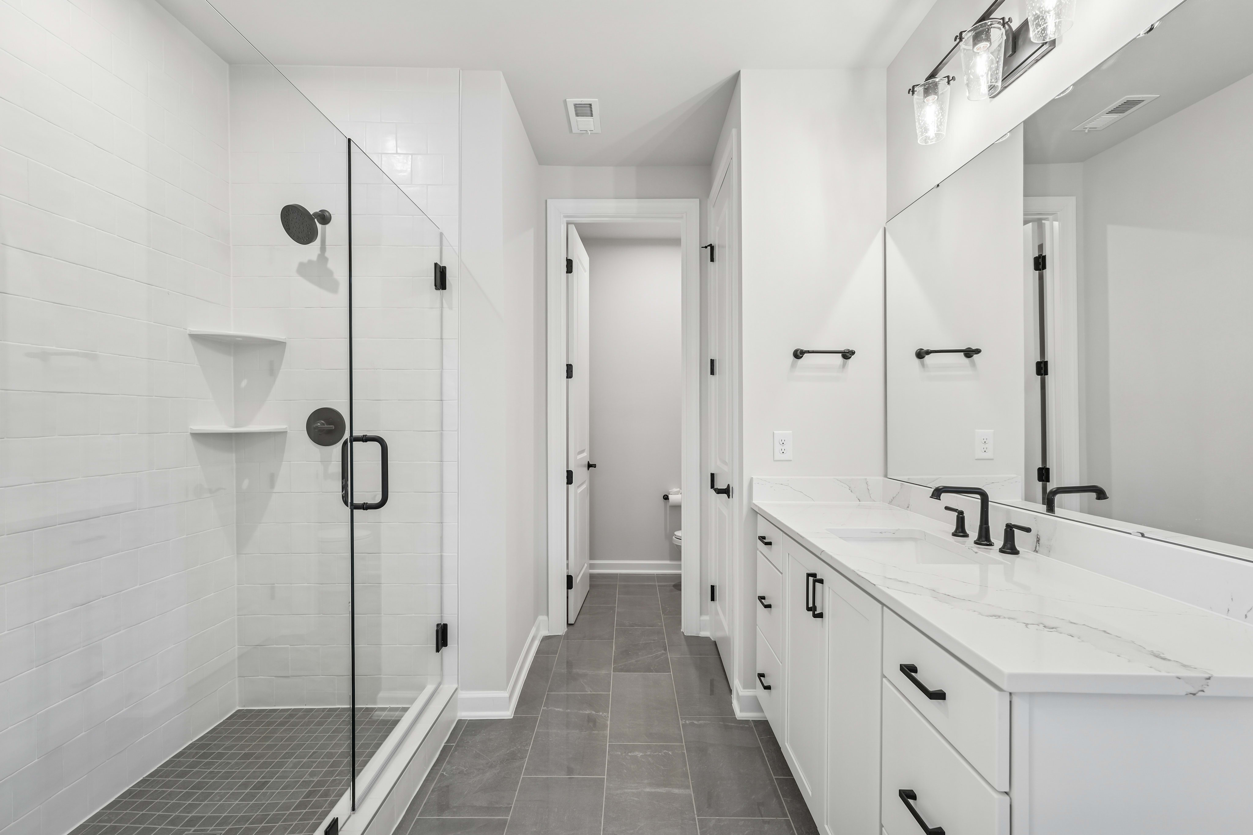 A modern, minimalist bathroom with white walls, a vanity with drawers, and a tiled floor leading to a hallway.