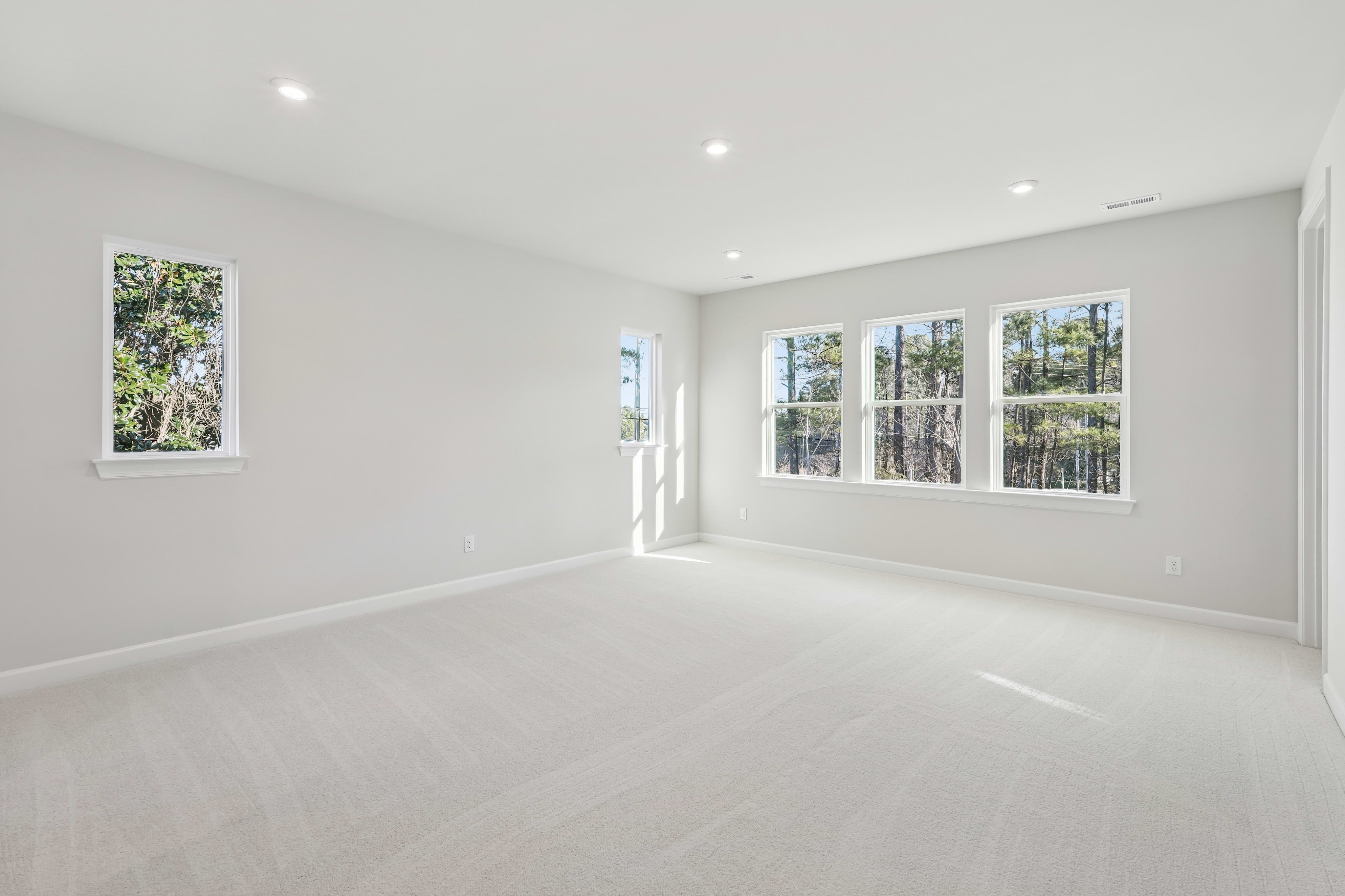 A bright, spacious room with large windows overlooking a lush, natural landscape, featuring a clean, minimalist design with hardwood floors and recessed lighting.