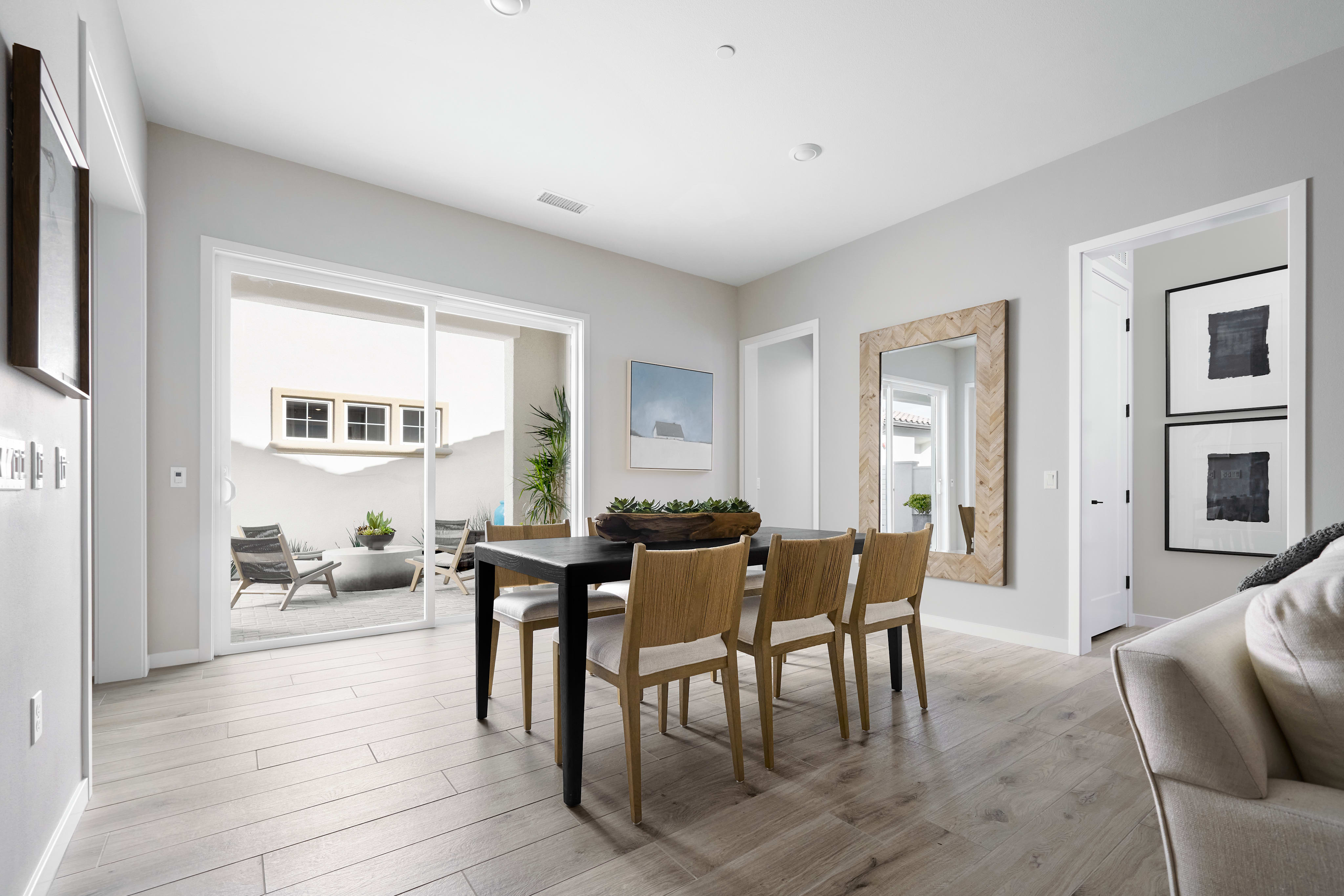 A modern and minimalist dining room with a wooden table and chairs, surrounded by light-colored walls and floors, and a large window providing natural light.