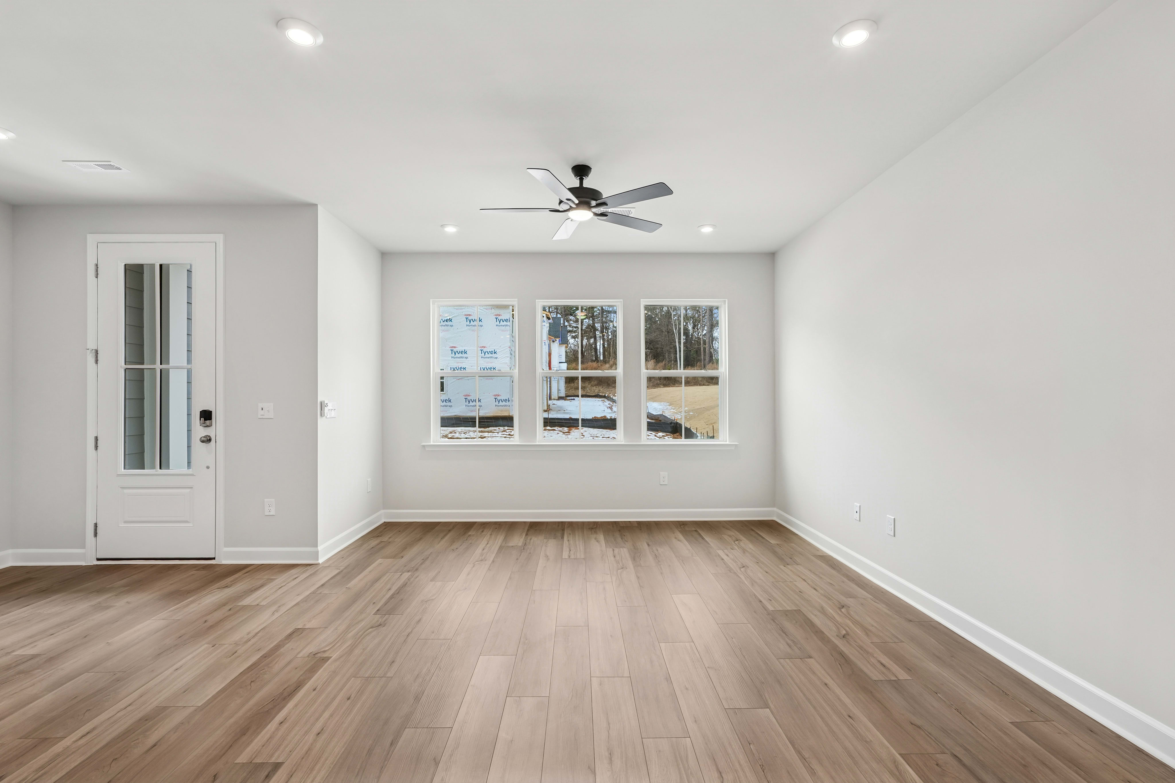 A bright, spacious room with a white wall, a ceiling fan, and a wooden floor.