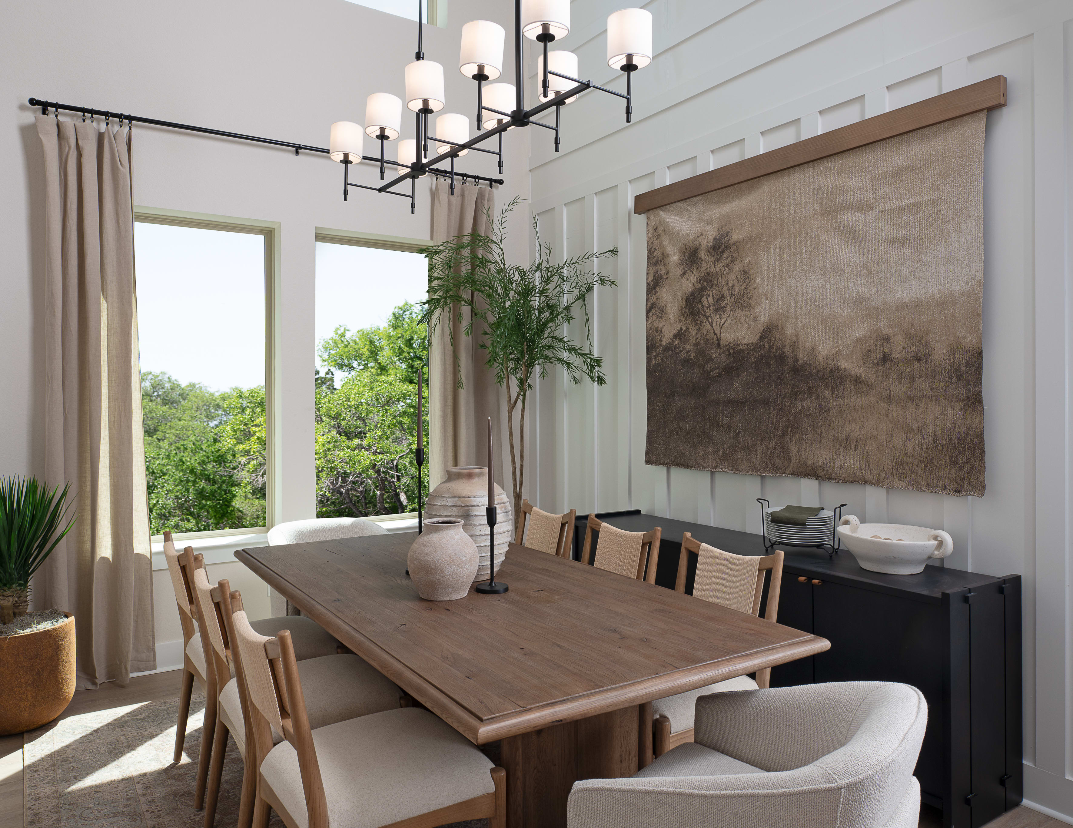 A spacious and modern dining room with a large wooden table, comfortable upholstered chairs, and a striking abstract artwork on the wall, complemented by a sleek black sideboard and a stylish chandelier overhead.