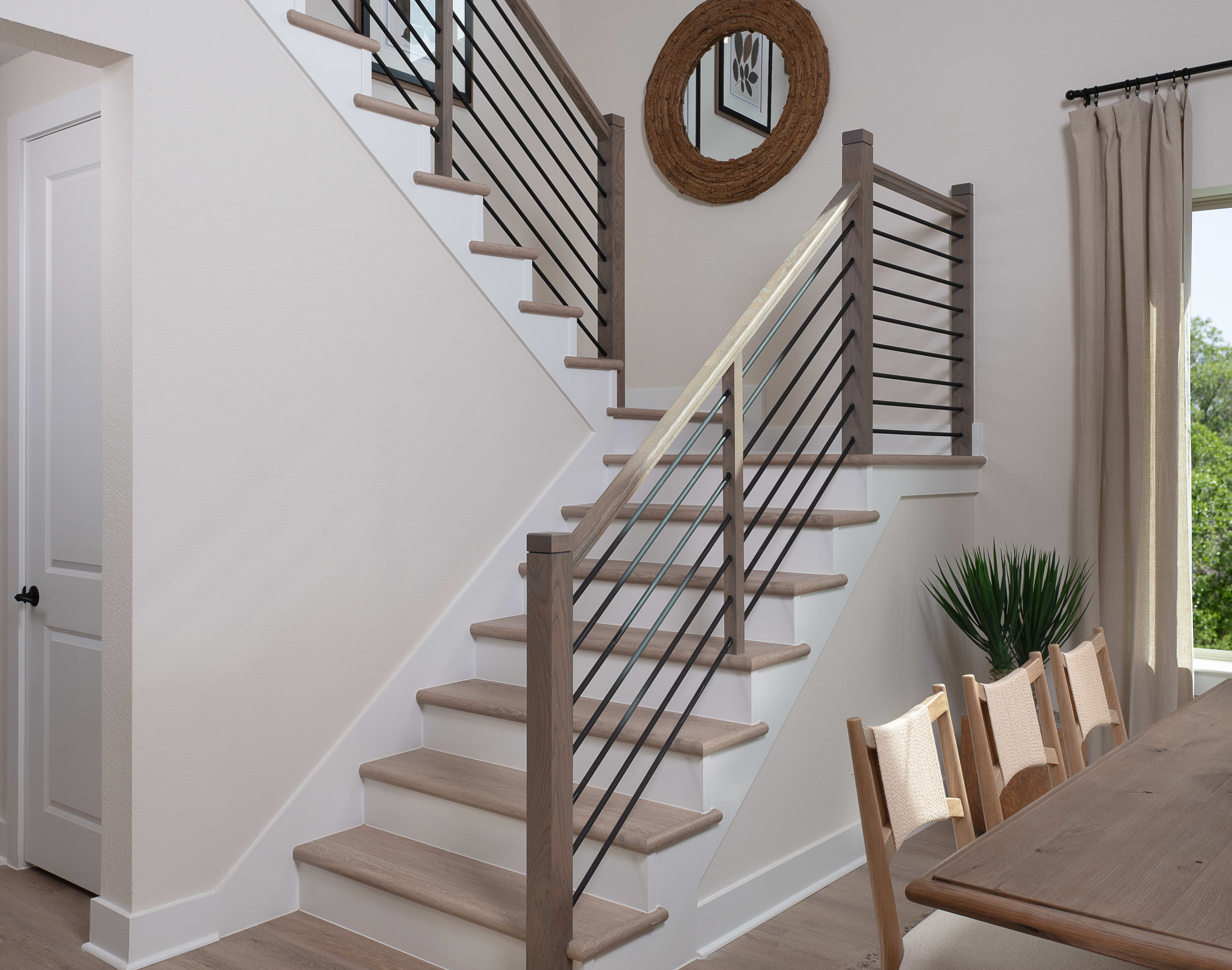 A modern and open-concept interior with a wooden staircase, minimalist railing, and a dining area visible in the background.