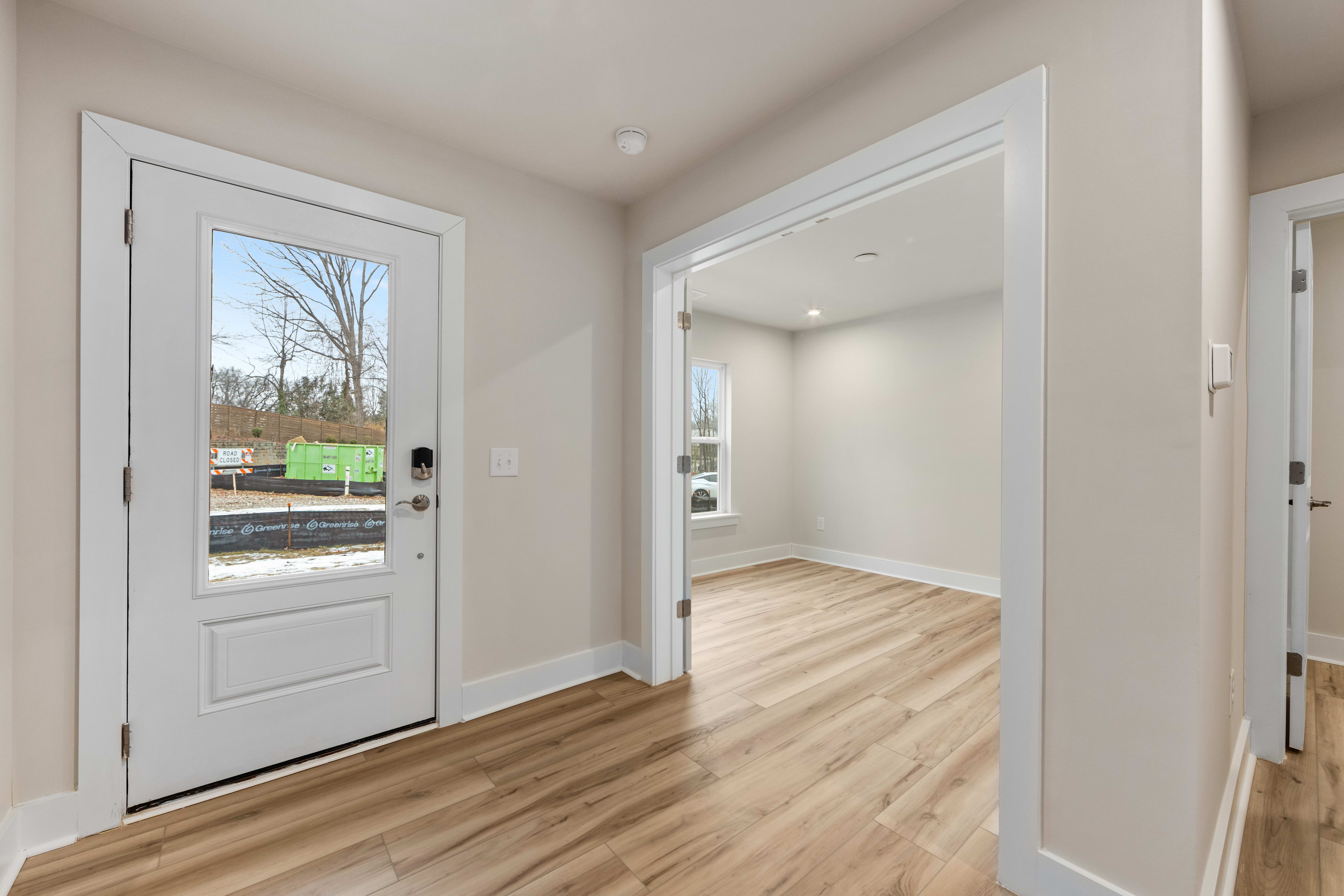 A bright and spacious entryway with a white front door, hardwood floors, and a view of the outdoors through the window.