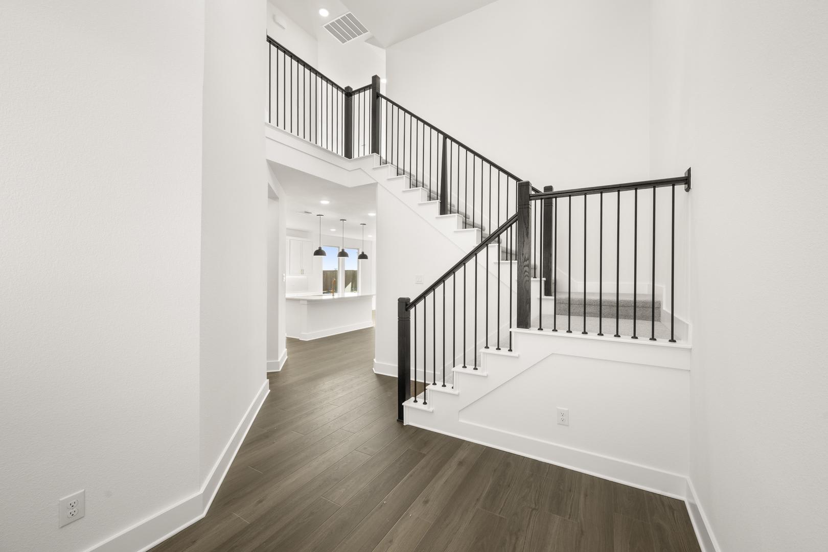 A modern, minimalist staircase with black metal railings leading up to a white-walled hallway, featuring a built-in shelving unit visible in the background.