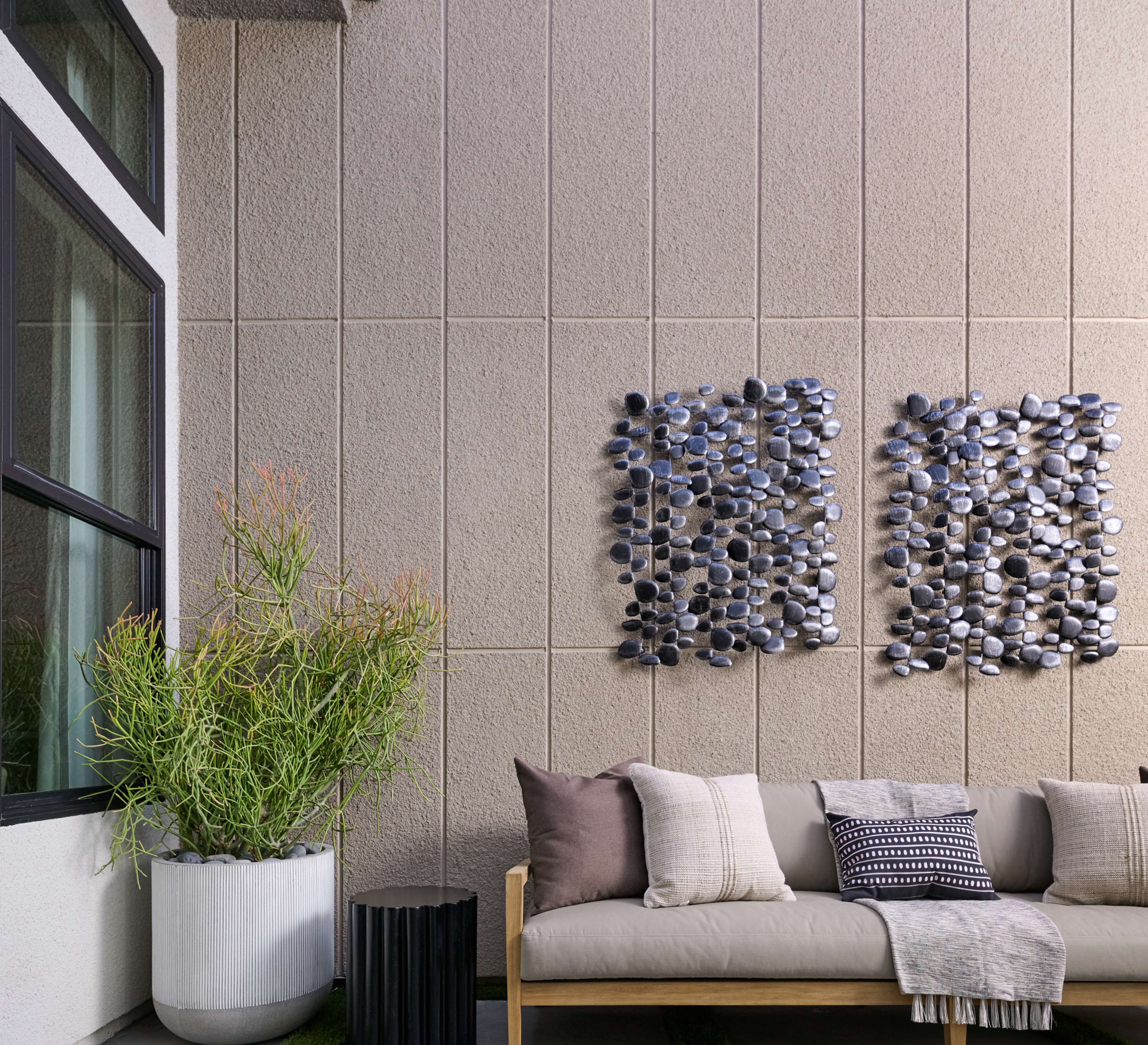A modern and minimalist outdoor living space with a couch, potted plants, and a textured wall feature.