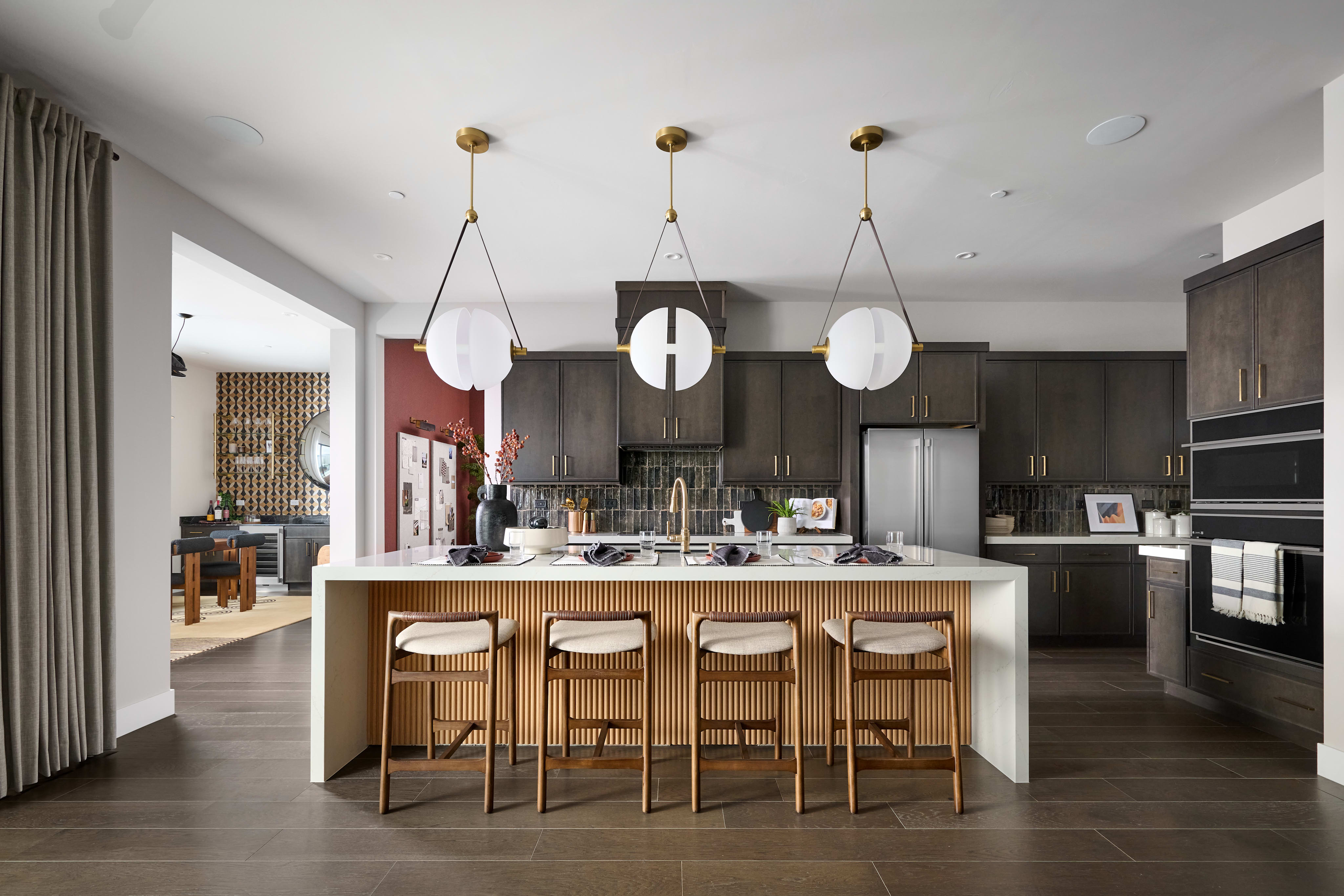 A modern and stylish kitchen with dark cabinets, a large island with bar stools, and pendant lights hanging from the ceiling.