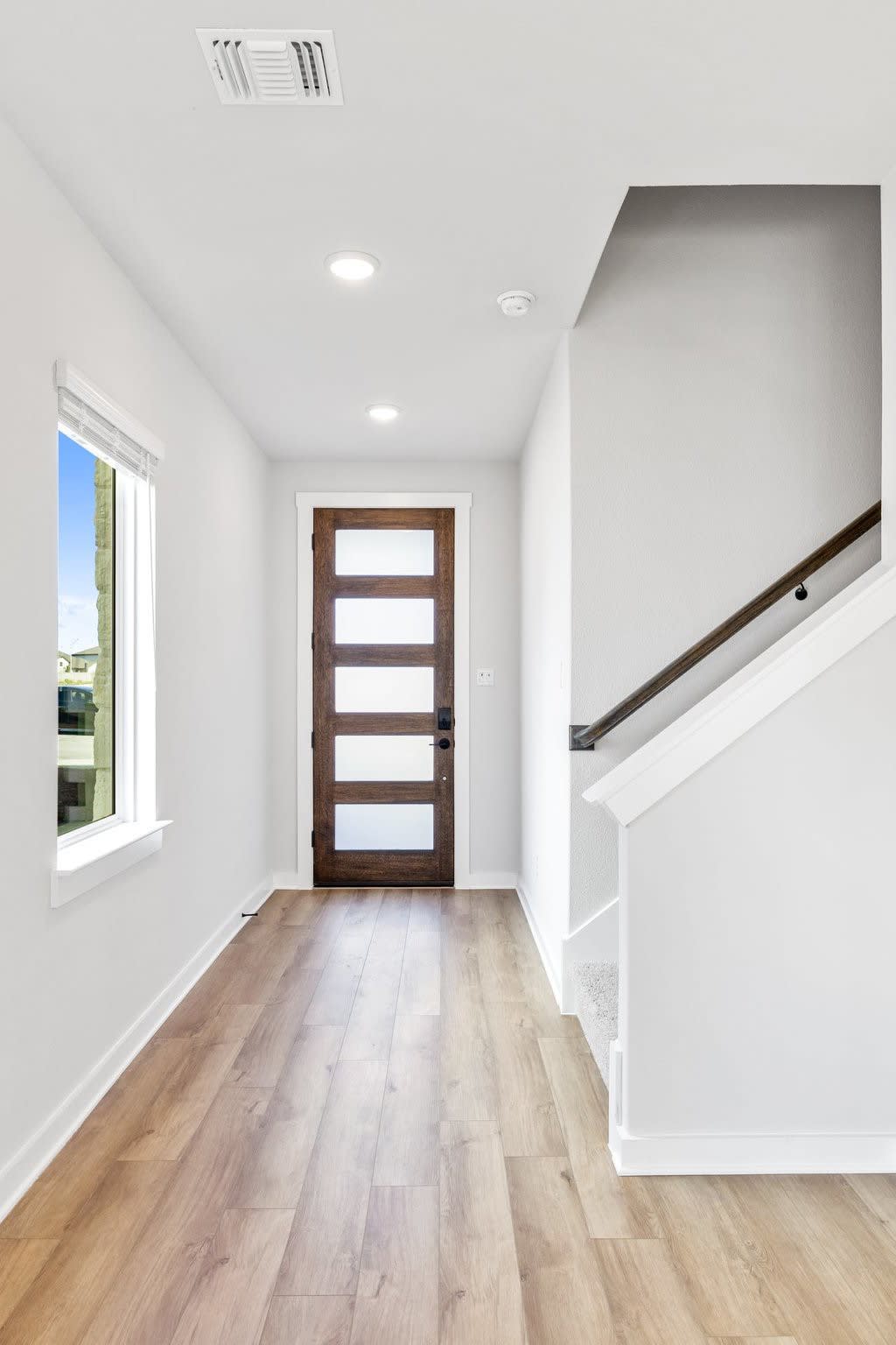 A bright, spacious entryway with a wooden door, hardwood floors, and a staircase leading to the upper level.