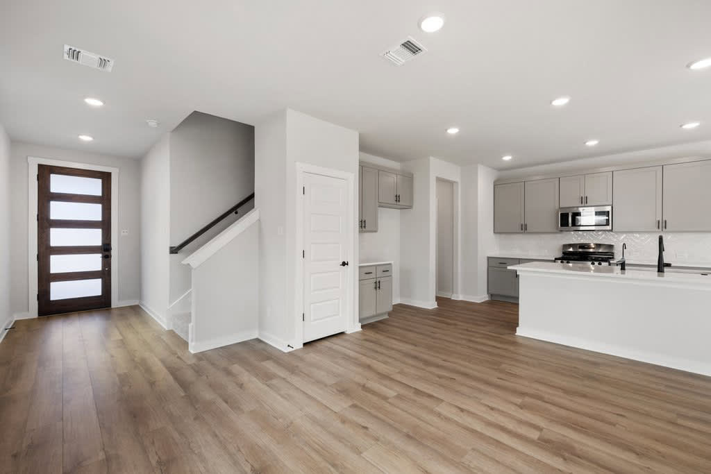 A modern, open-concept kitchen and living space with white walls, hardwood floors, and recessed lighting.