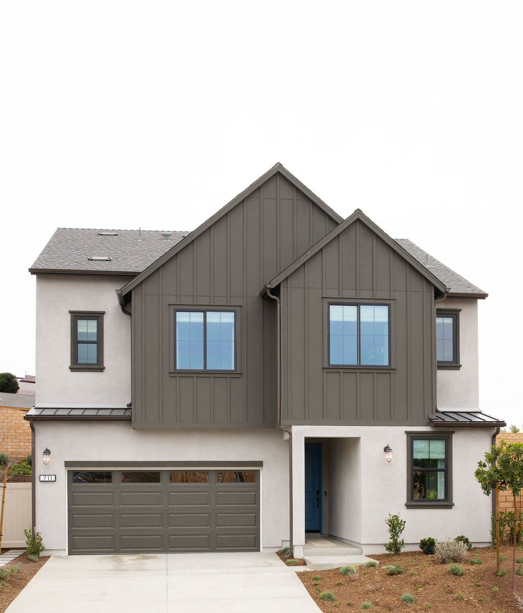 A two-story residential house with a gray exterior, a garage door, and several windows overlooking a grassy yard.