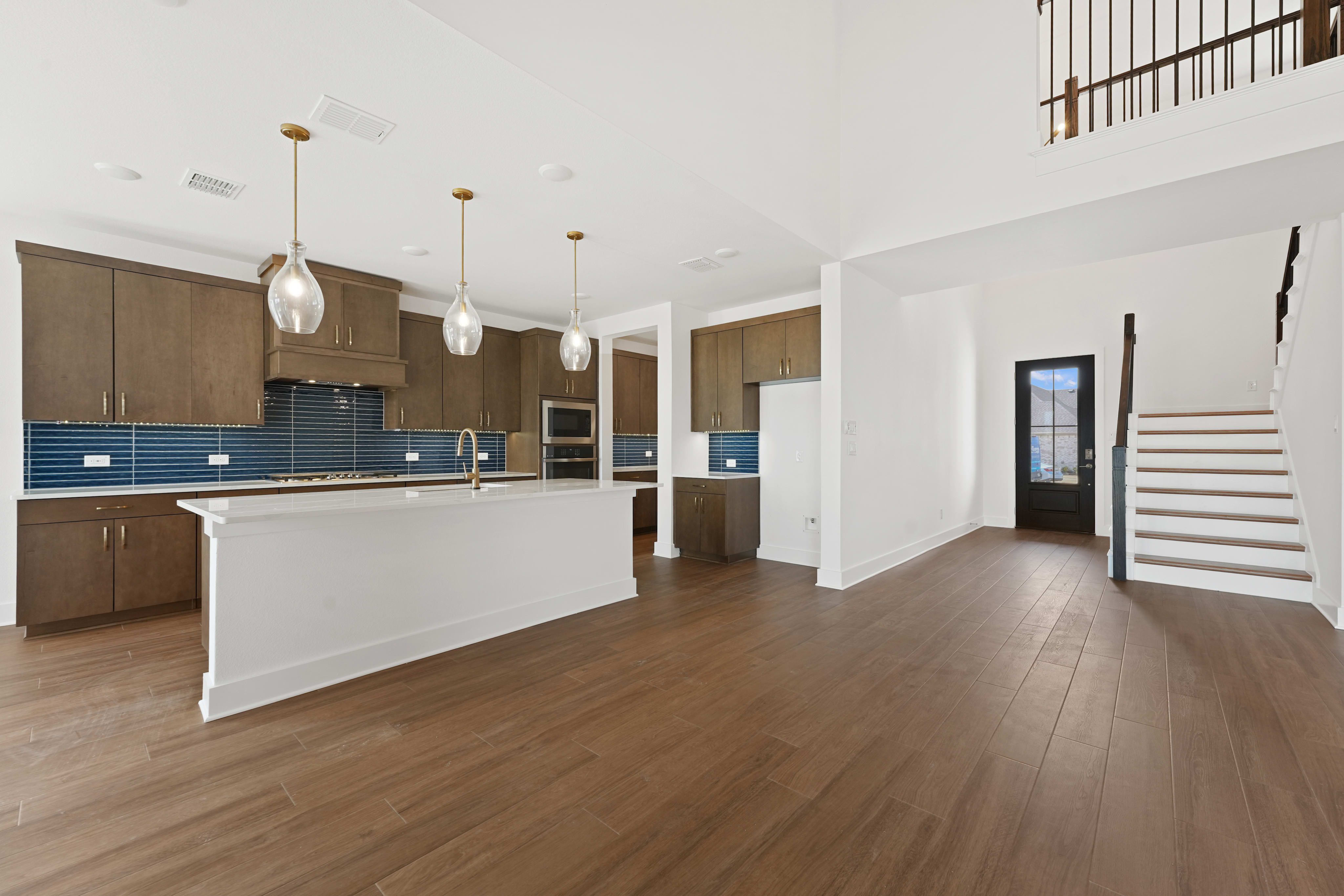 A modern, open-concept kitchen and living space with wooden floors, white walls, and pendant lighting fixtures.