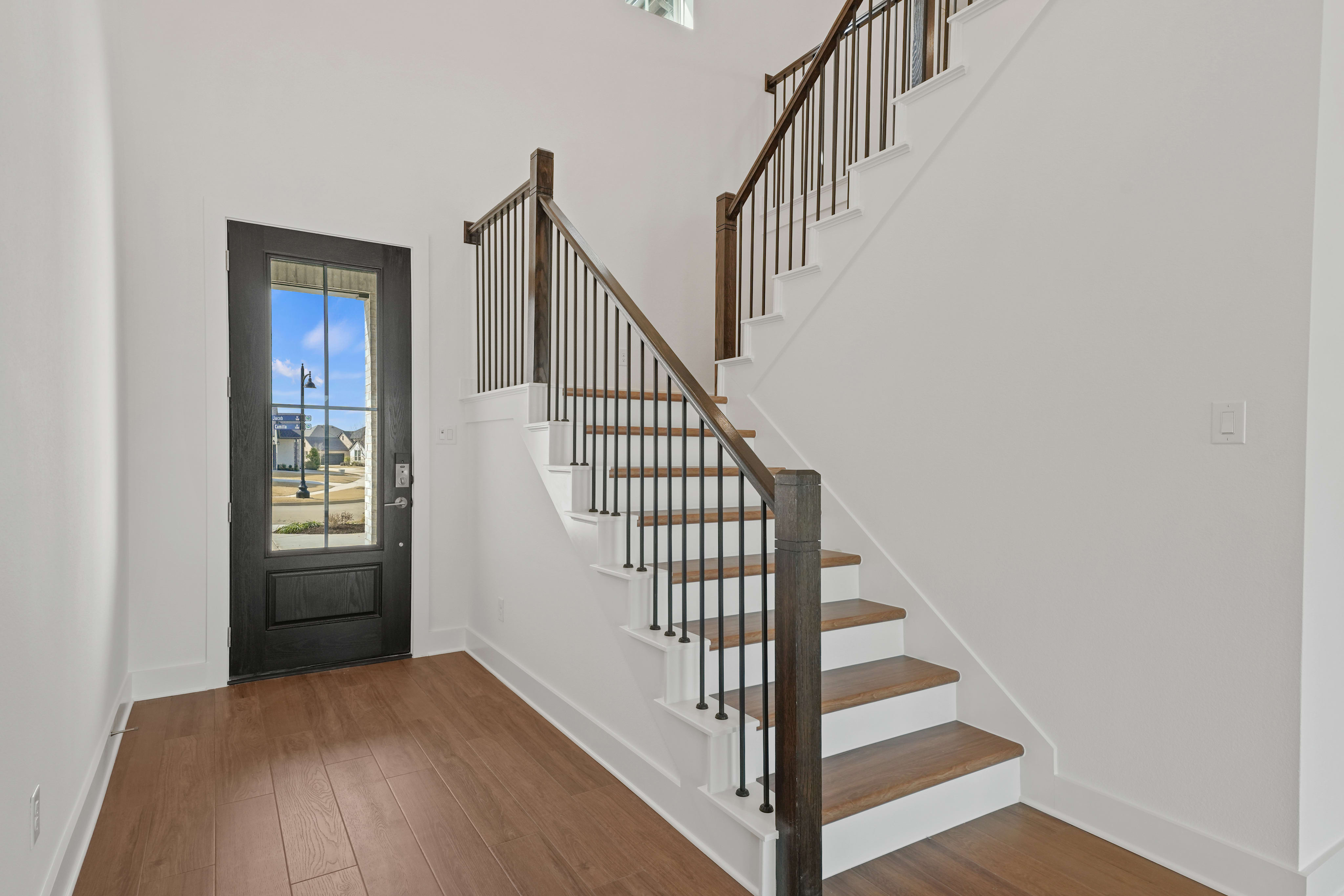 A modern, well-lit entryway with a wooden staircase, metal railings, and a glass door leading to an outdoor area.