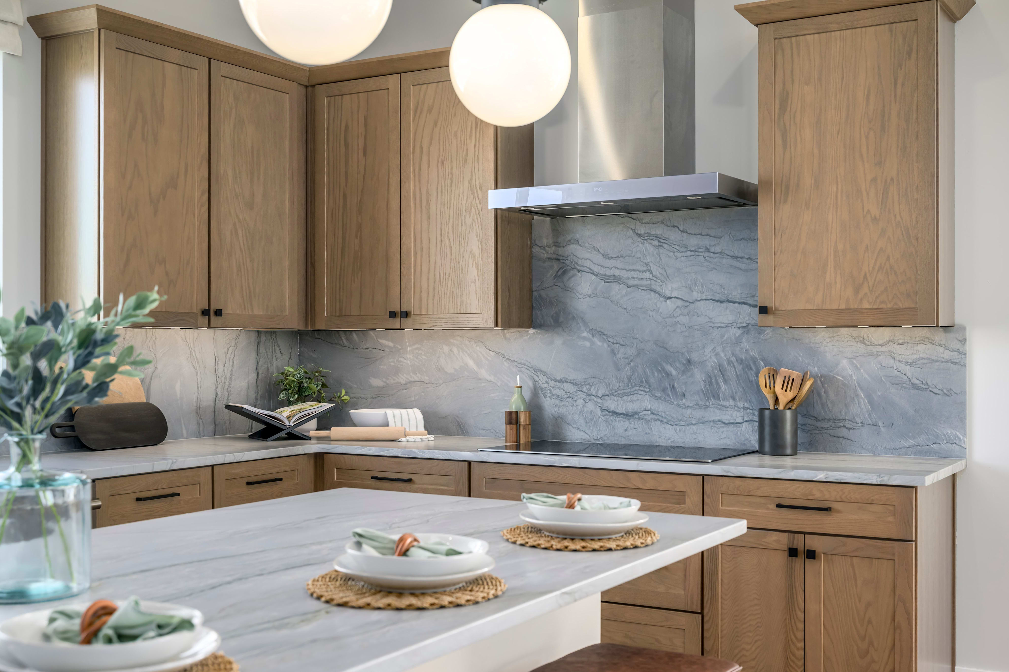 A modern and minimalist kitchen with wooden cabinets, a marble backsplash, and a central island with baked goods displayed on it.