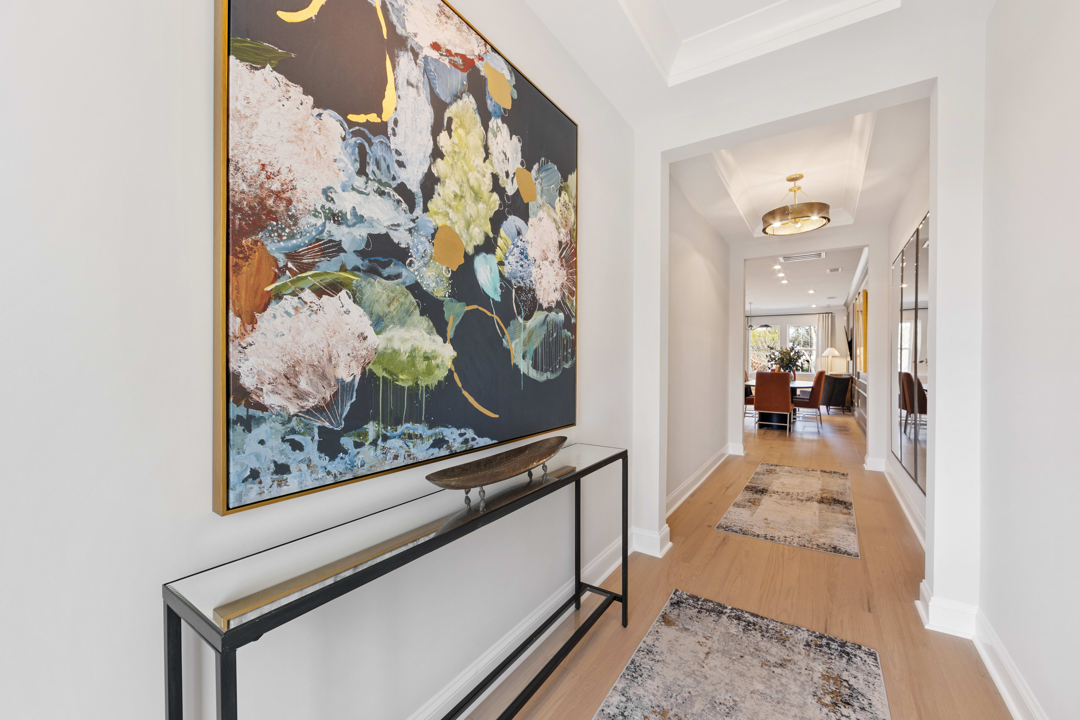 A vibrant floral painting adorns the wall in the hallway, leading the eye down the wooden-floored corridor towards a room in the background.