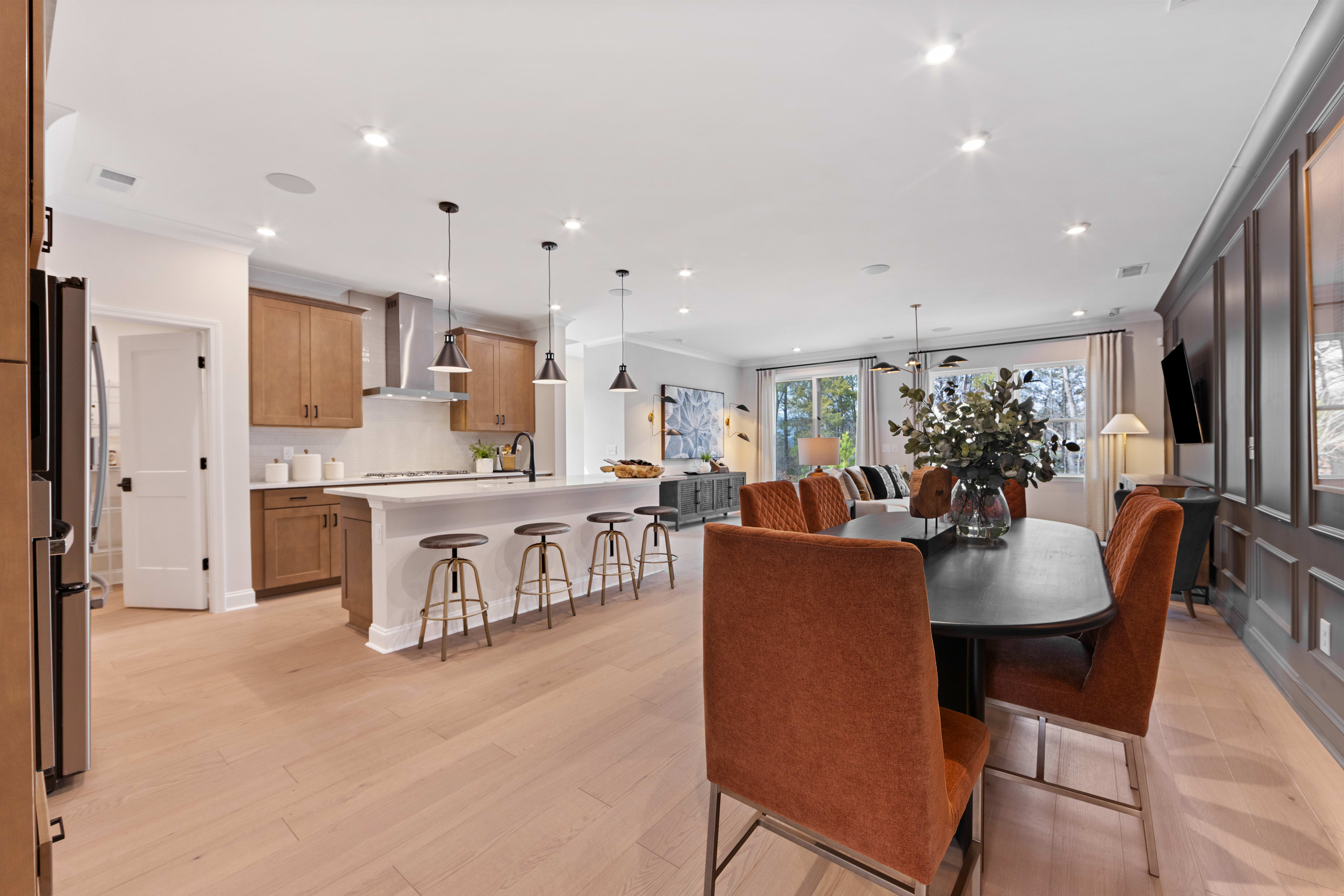 A modern and spacious open-concept kitchen and dining area with wooden cabinets, a large dining table, and pendant lighting fixtures.