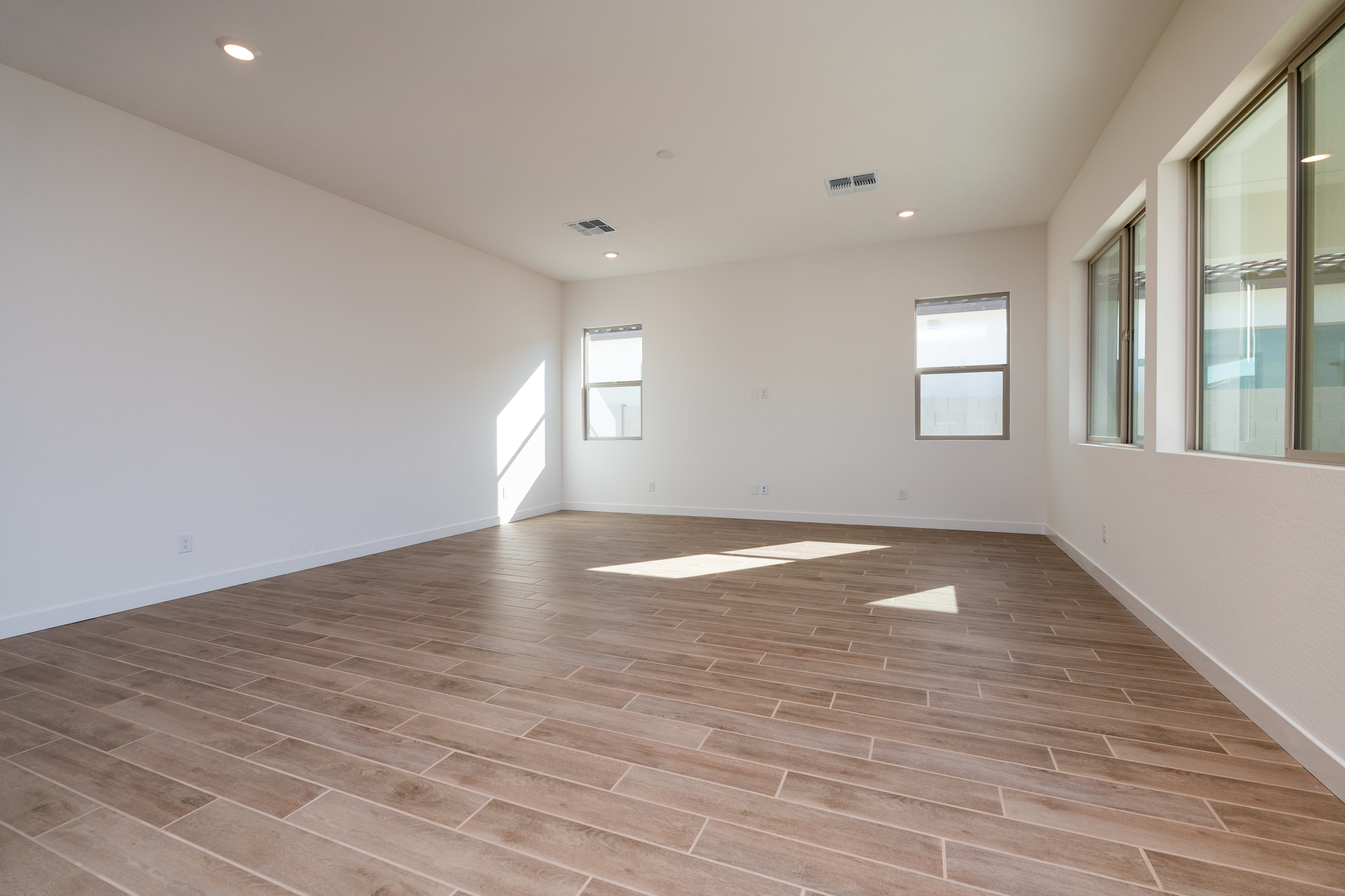 An empty, well-lit room with a hardwood floor and large windows, creating a bright and spacious atmosphere.