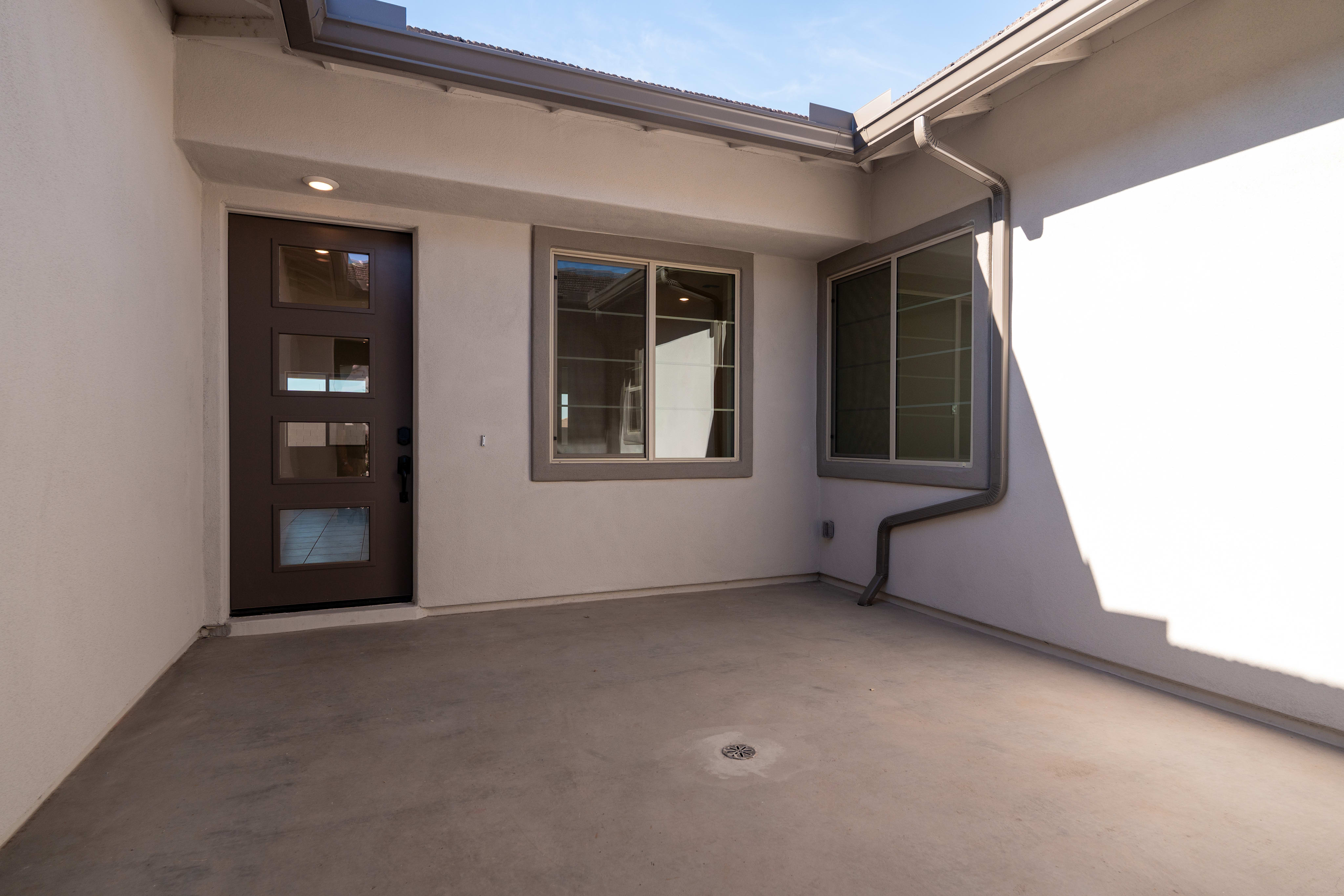A covered patio or entryway with a dark wooden door, windows, and a concrete floor.