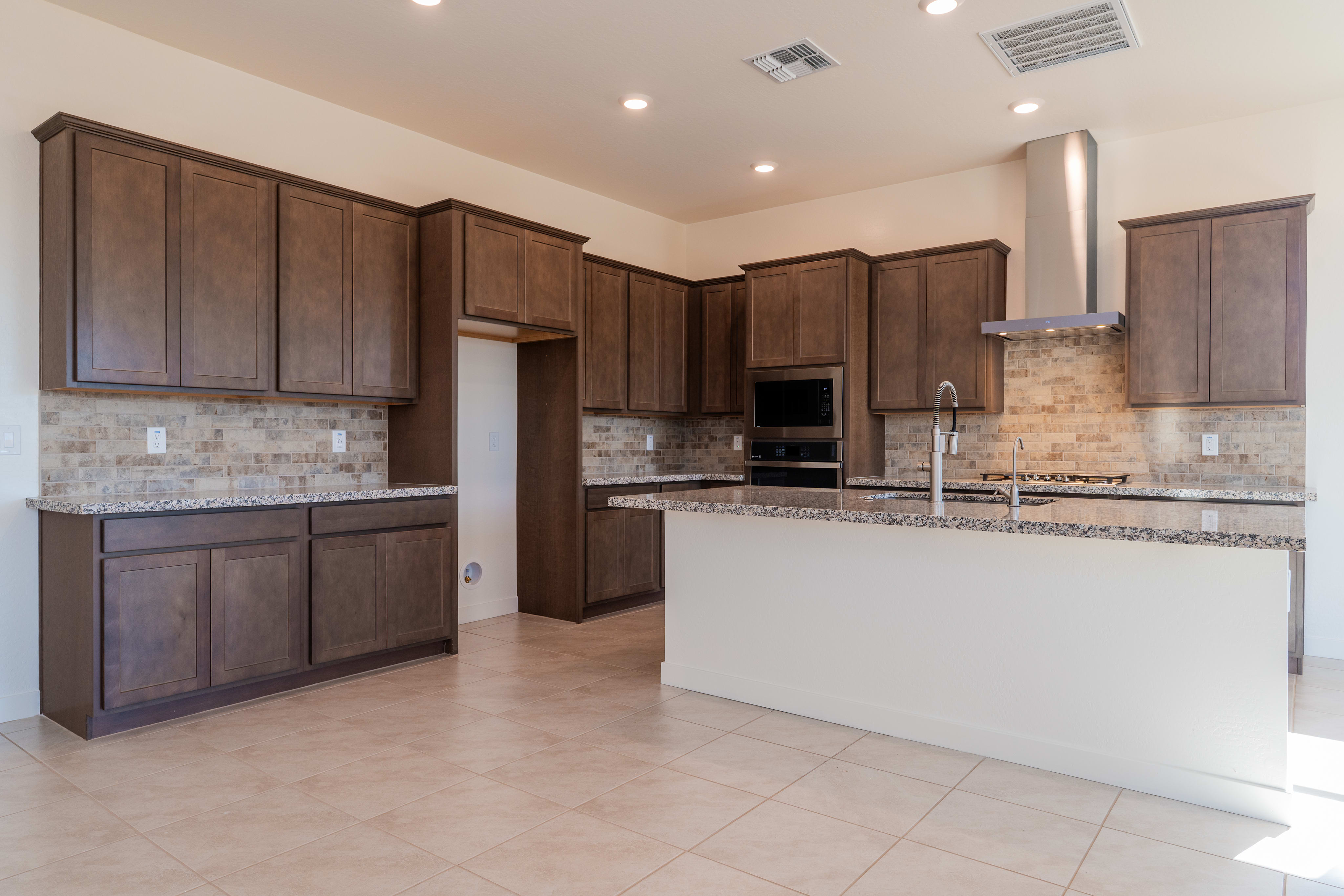 A modern kitchen with dark wood cabinets, granite countertops, and a tiled backsplash, set against a bright and open space.