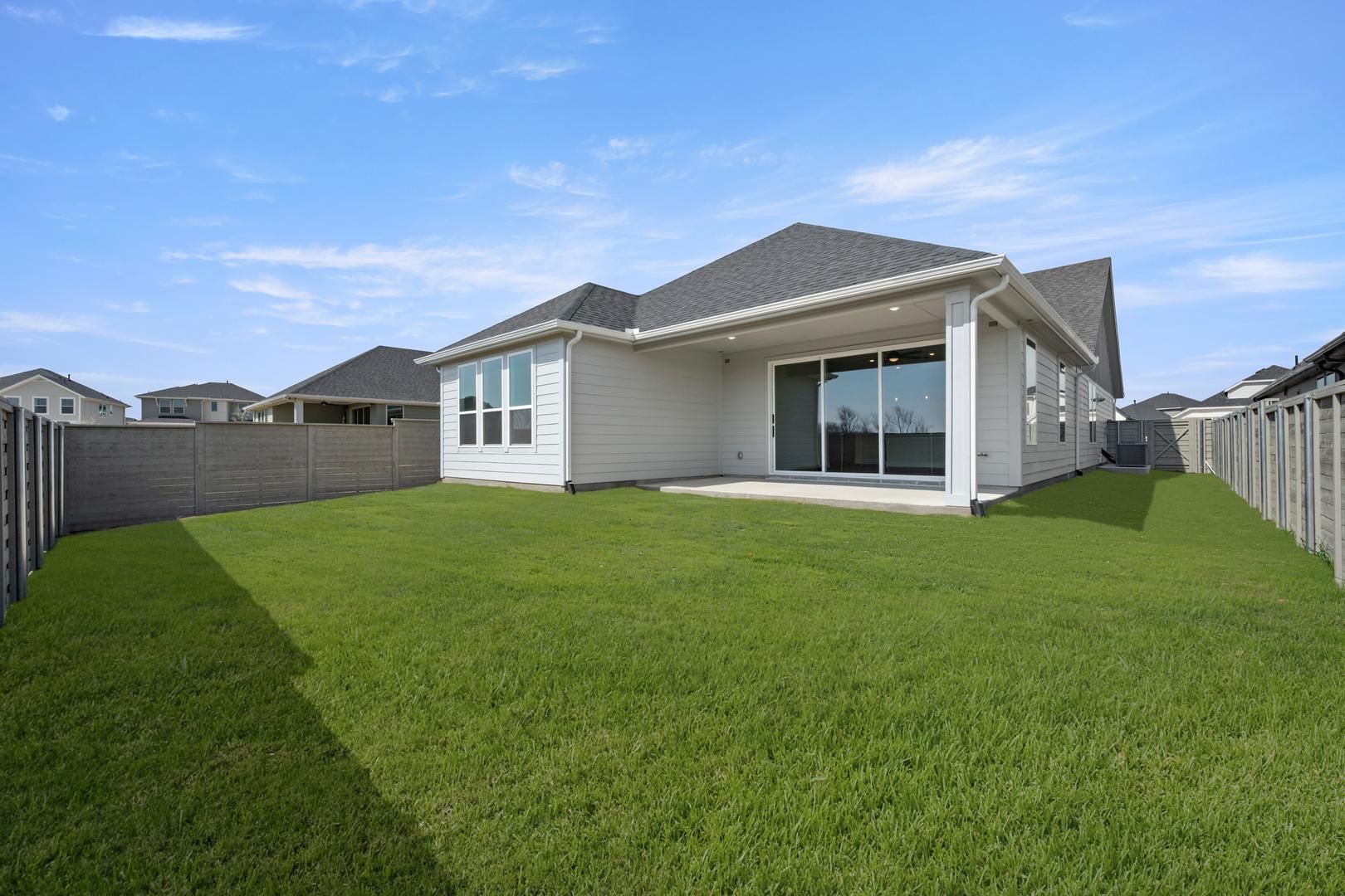 A well-manicured lawn surrounds a modern, single-story house with a gray roof and white siding, set against a clear blue sky with scattered clouds.