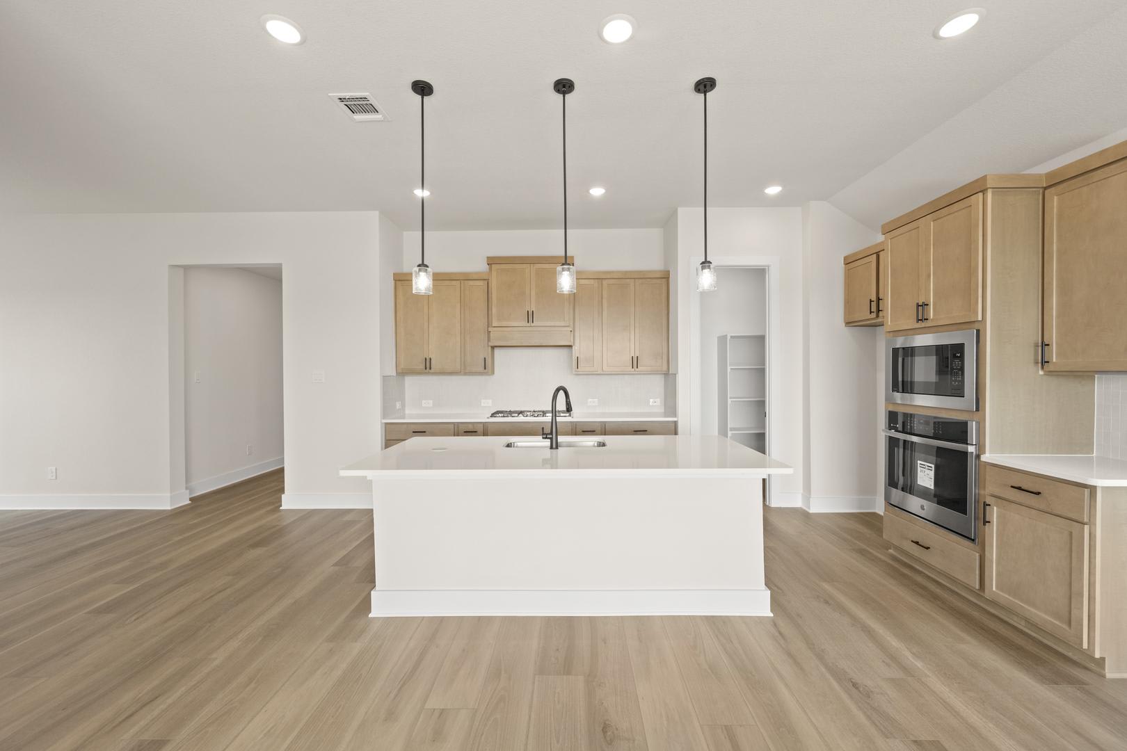 A modern, open-concept kitchen with light wood cabinets, a white island, and hardwood floors, illuminated by pendant lights.