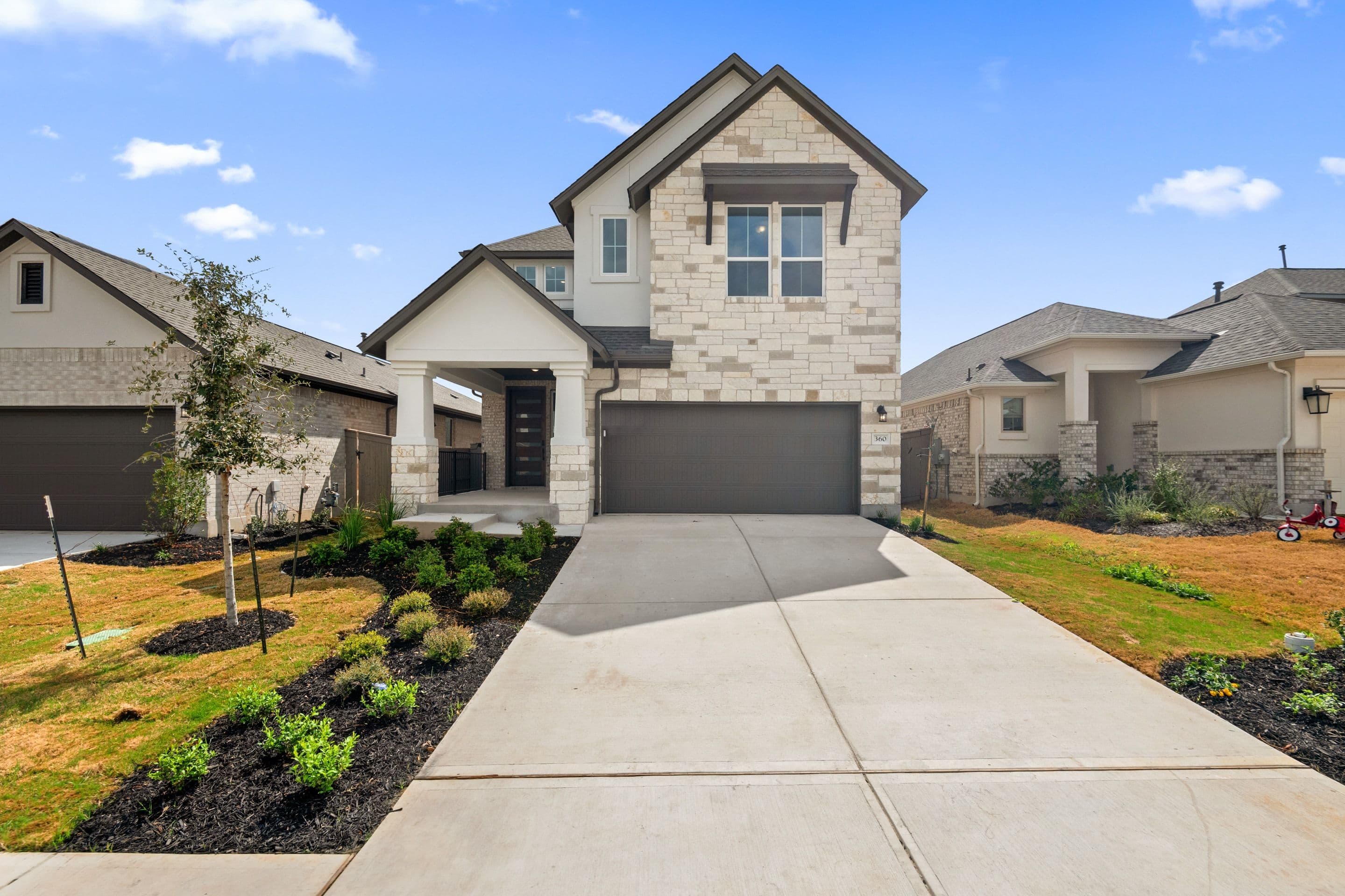 A modern two-story house with a stone exterior, a garage, and a well-landscaped front yard with a concrete walkway leading to the entrance.