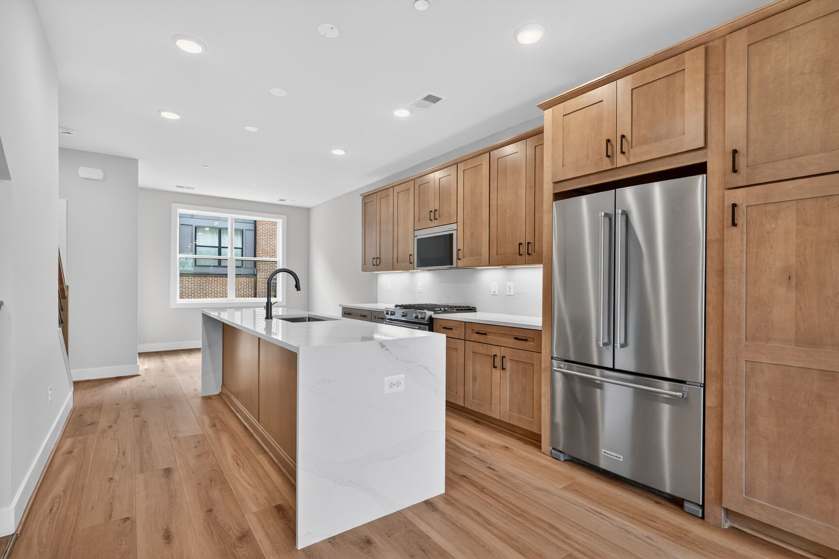 A modern, well-lit kitchen with wooden cabinets, stainless steel appliances, and a white countertop extending into a breakfast bar.