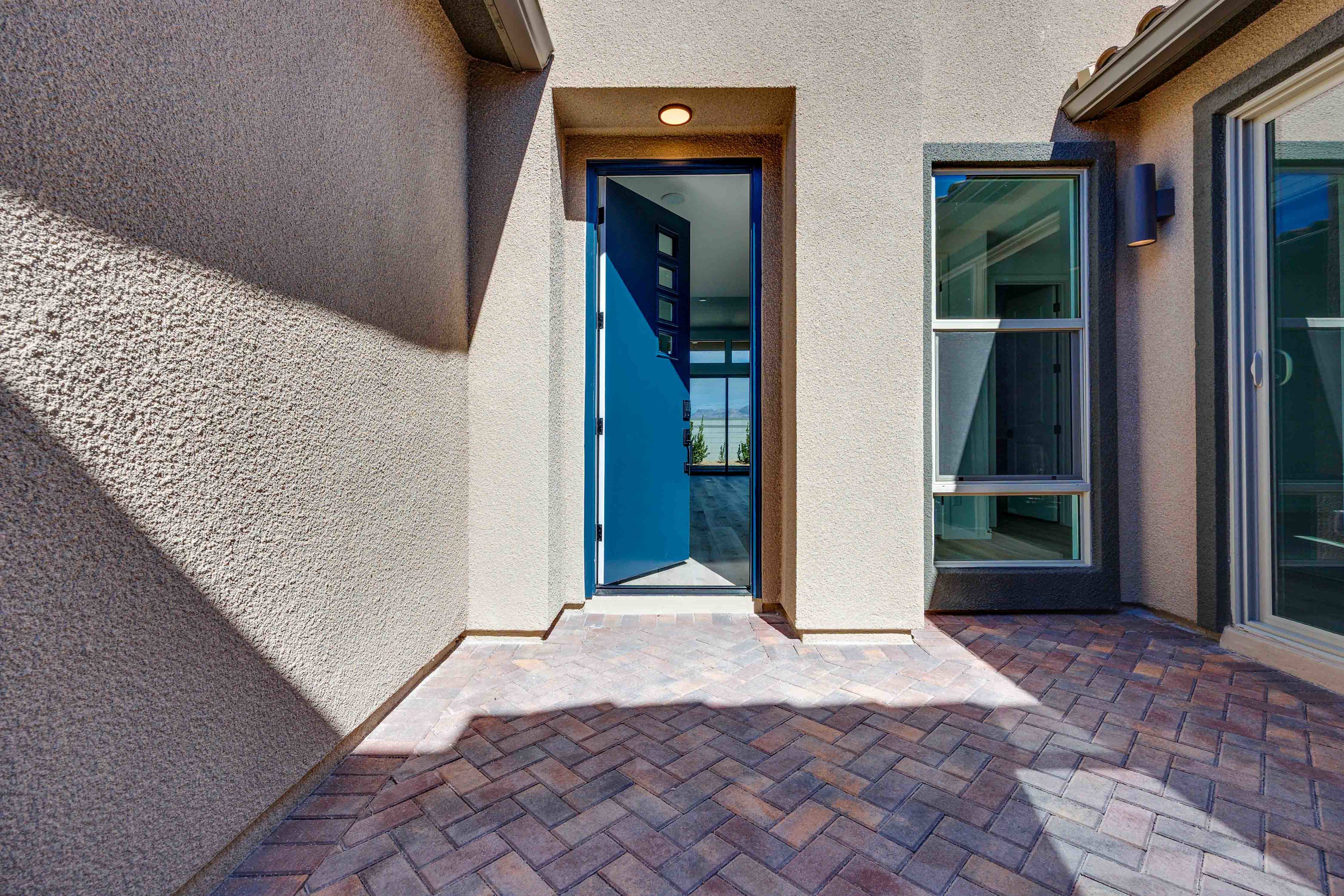 A brick-paved entryway leads to a glass-paneled door, with a wall-mounted light fixture and a textured exterior wall visible in the background.