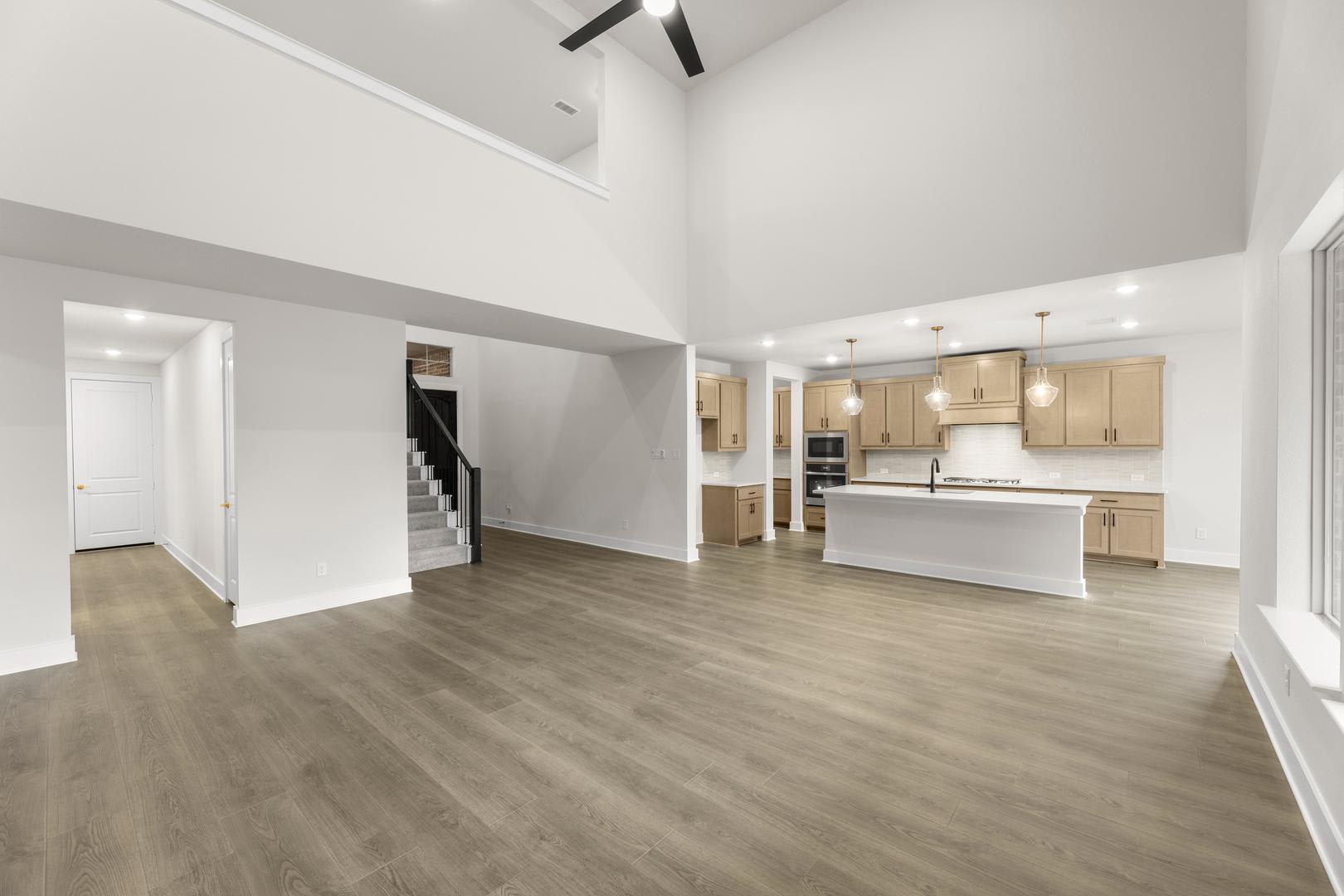 A spacious and modern open-plan living area with a kitchen, hardwood floors, and high ceilings.