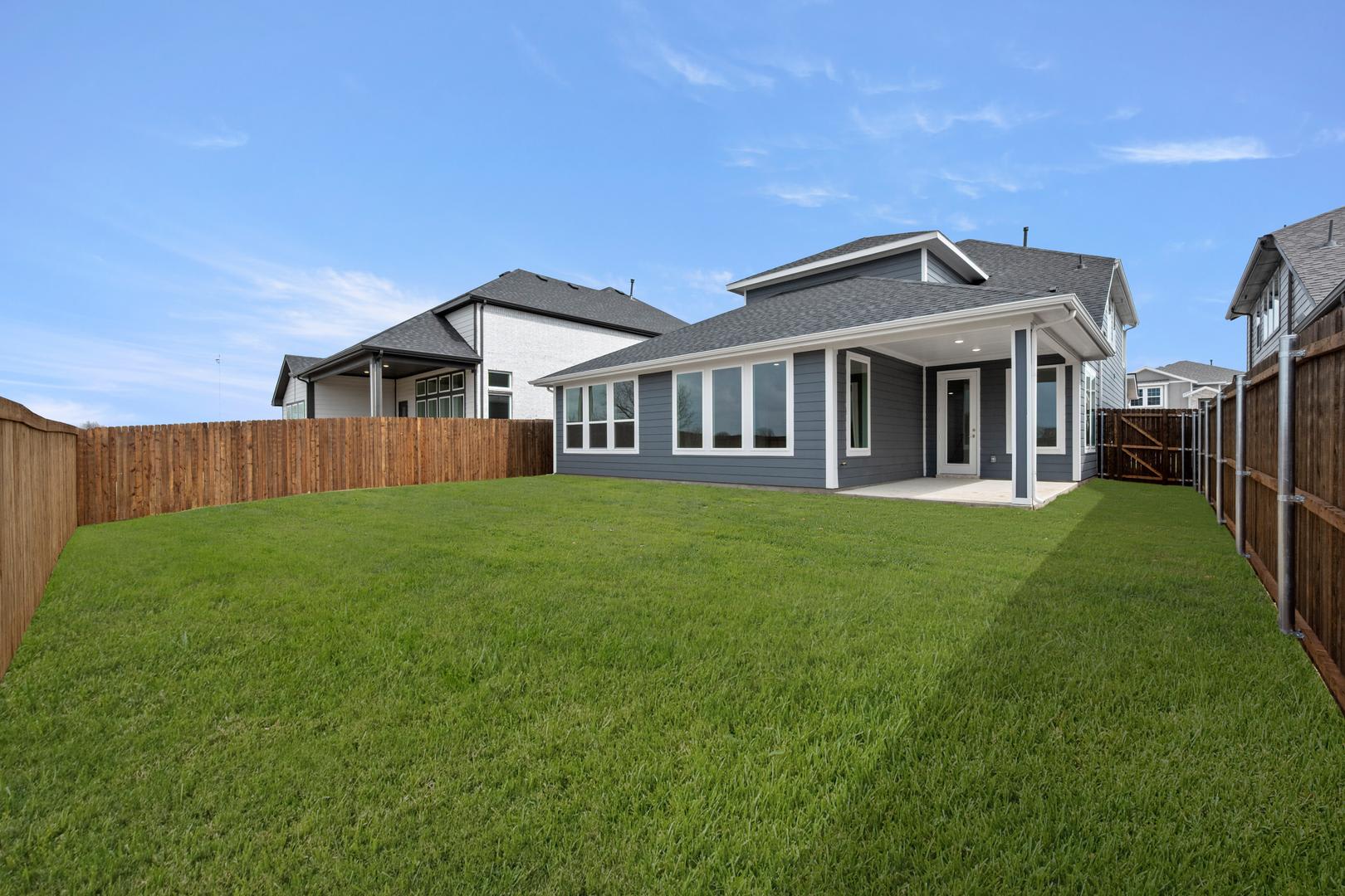 A well-manicured lawn stretches out in the foreground, leading to a modern, two-story house with a porch and large windows in the background.