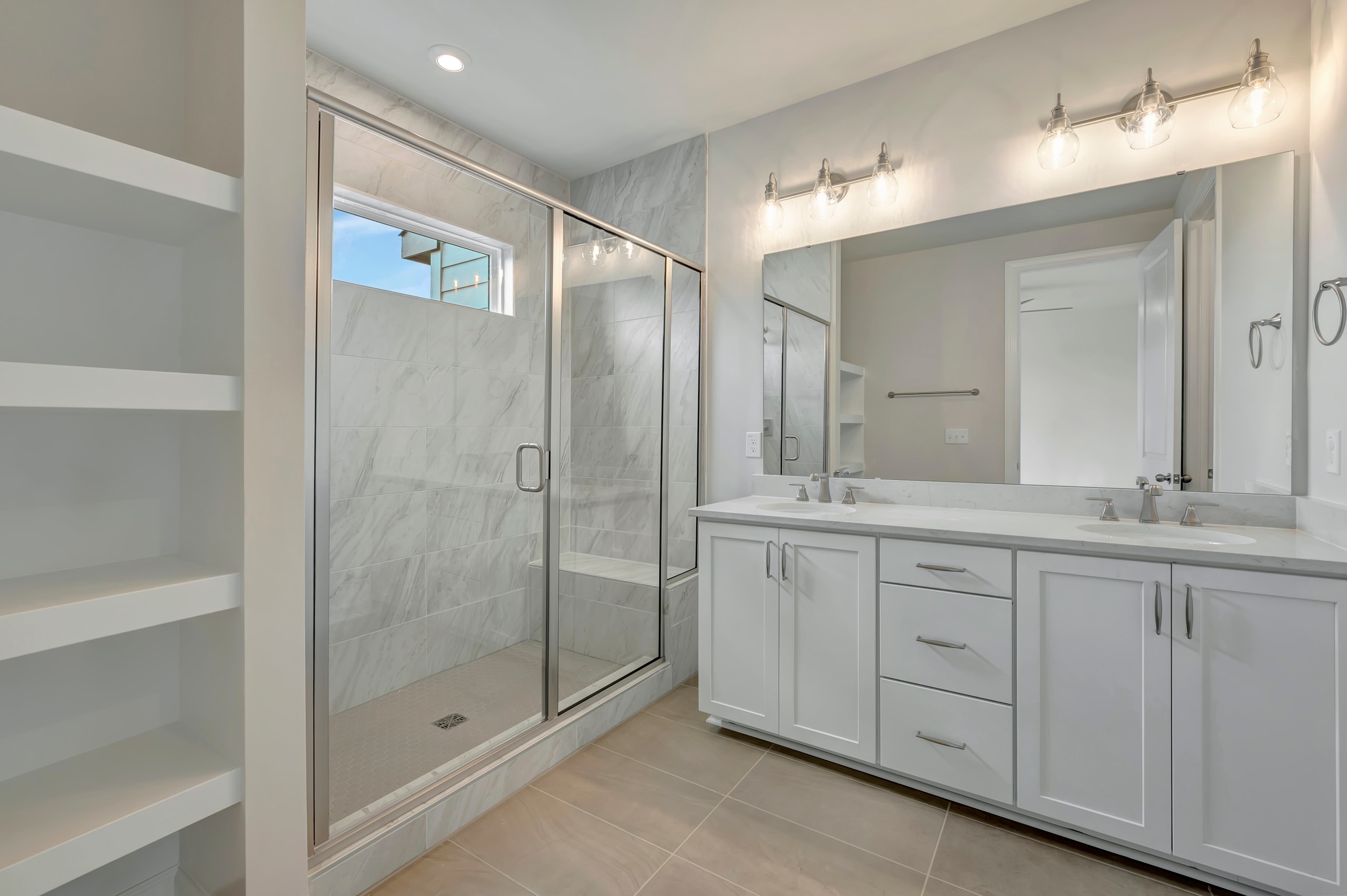 A modern, well-lit bathroom with a glass-enclosed shower, a vanity with drawers, and a large mirror on the wall.