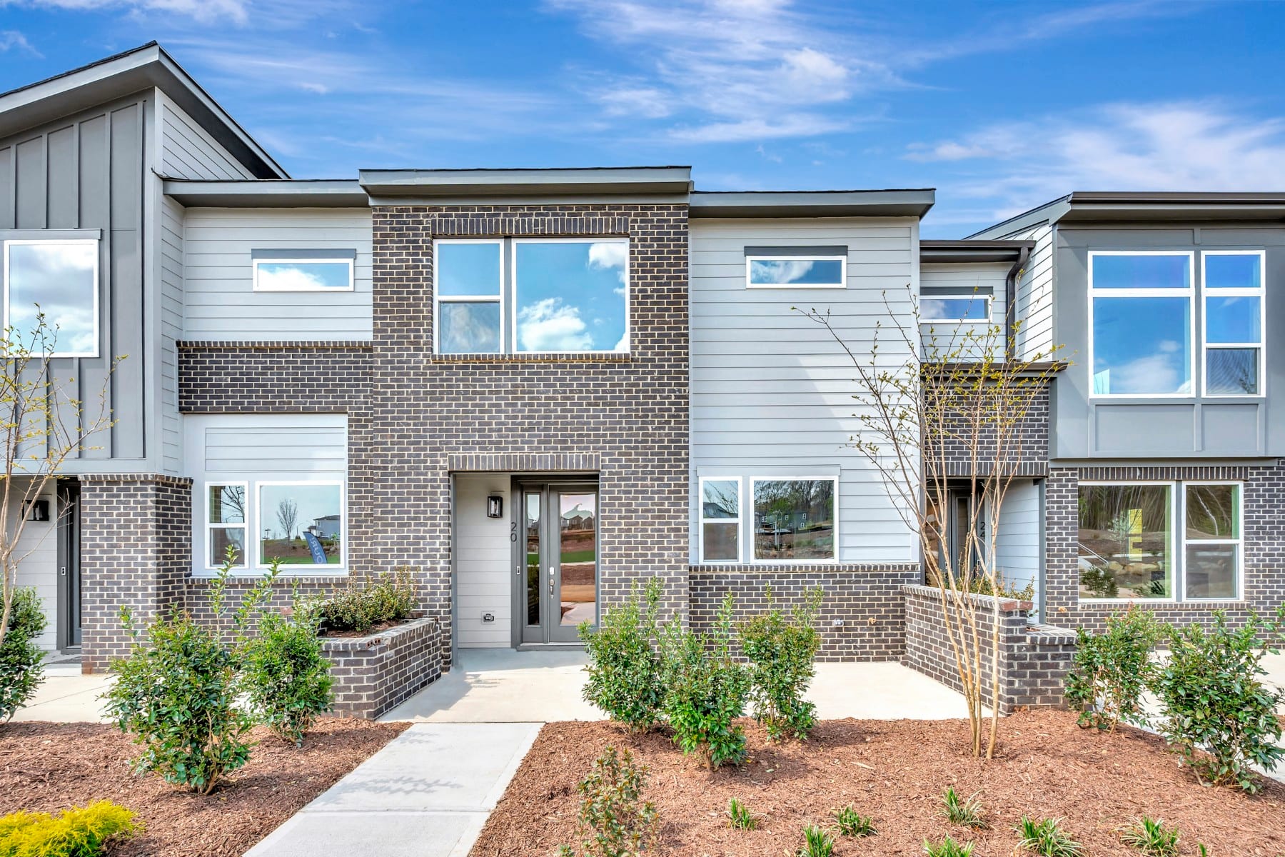 A modern two-story townhouse with a brick exterior, surrounded by landscaped gardens and a clear blue sky in the background.