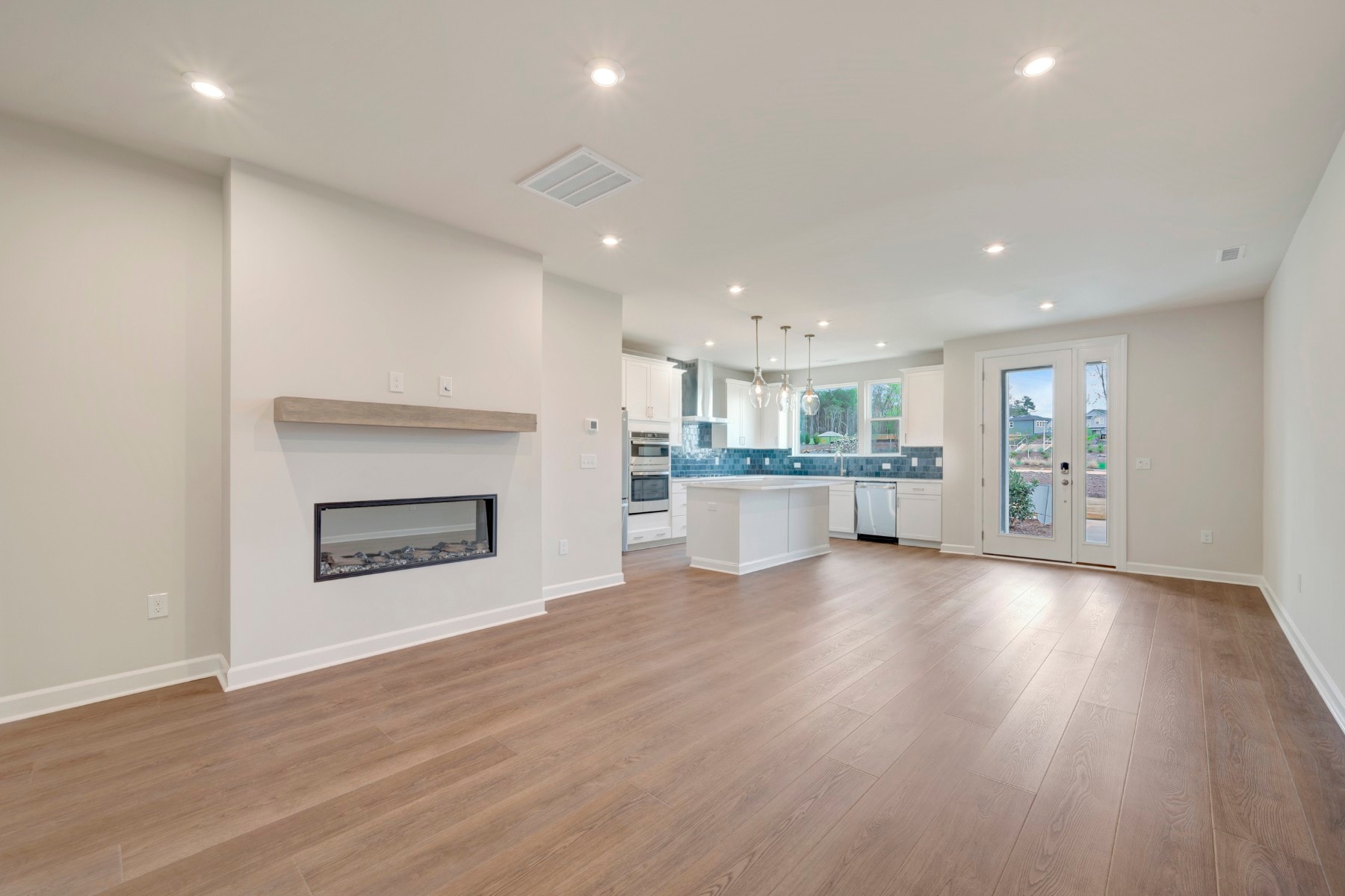A modern, open-concept living space with a fireplace, hardwood floors, and a well-equipped kitchen visible in the background.