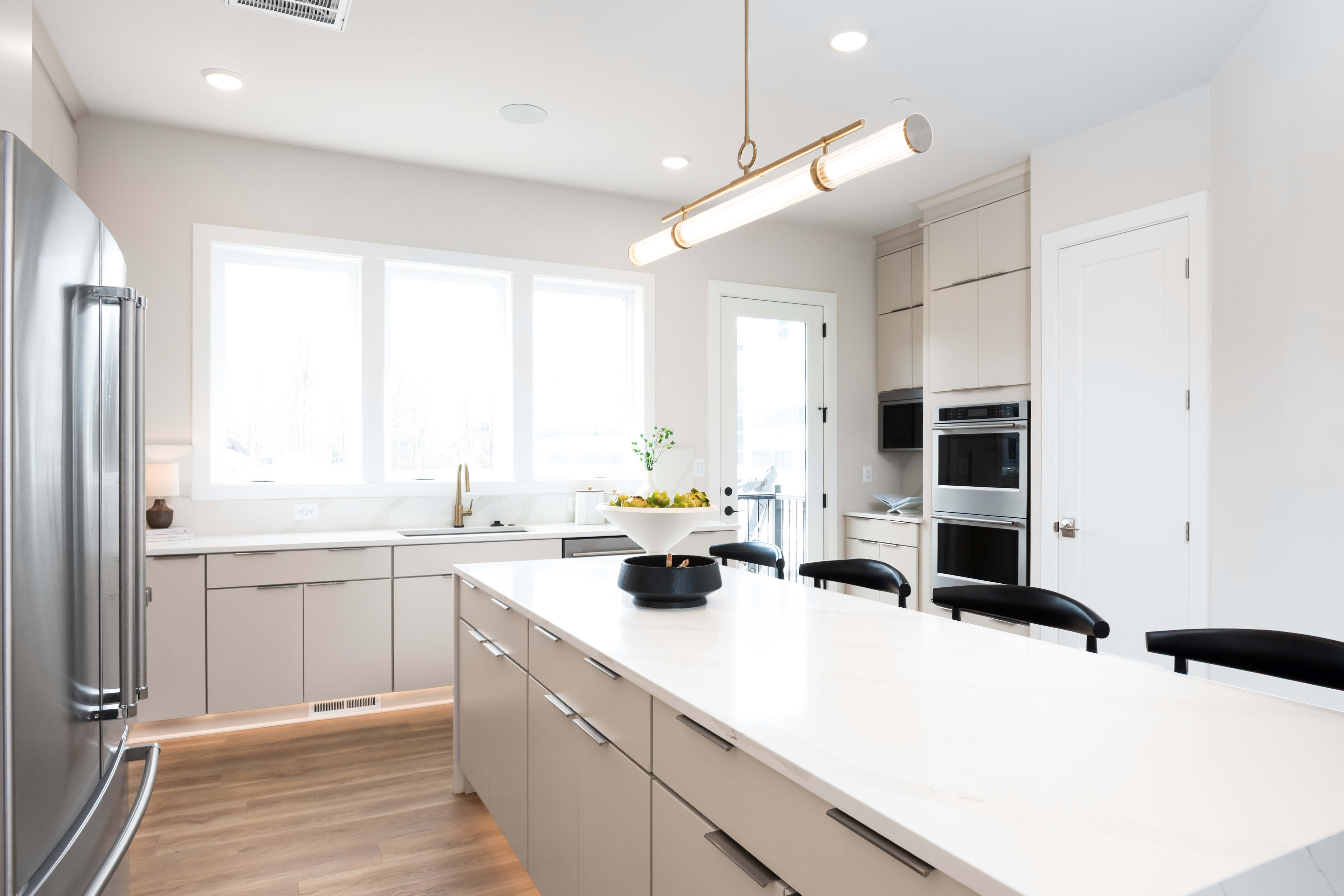 A modern, bright kitchen with white cabinets, a large countertop, and a stainless steel refrigerator visible in the background.