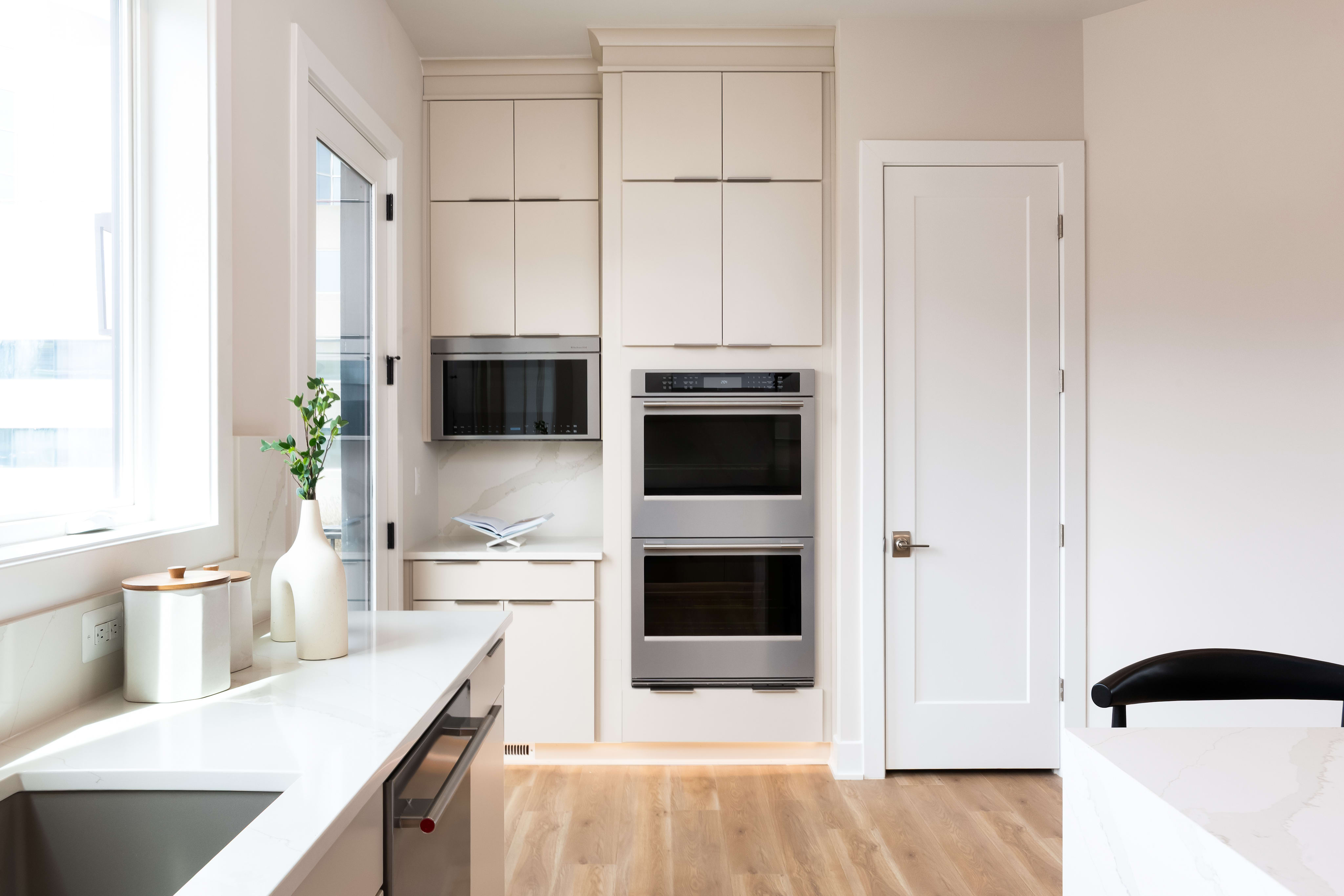 A modern, minimalist kitchen with white cabinets, stainless steel appliances, and a wooden floor.