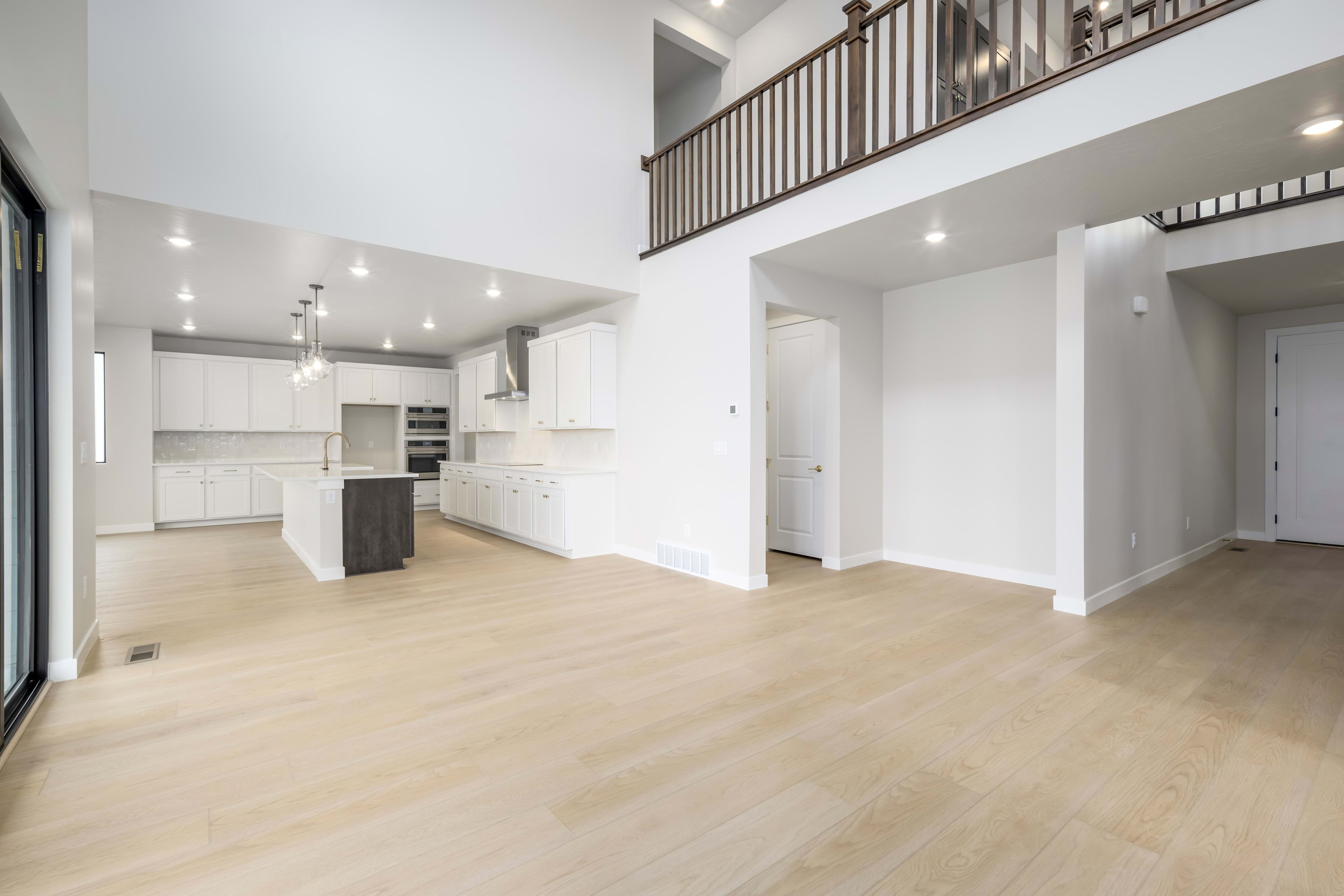 A spacious and modern open-concept living space with a kitchen, hardwood floors, and a second-floor balcony overlooking the main area.