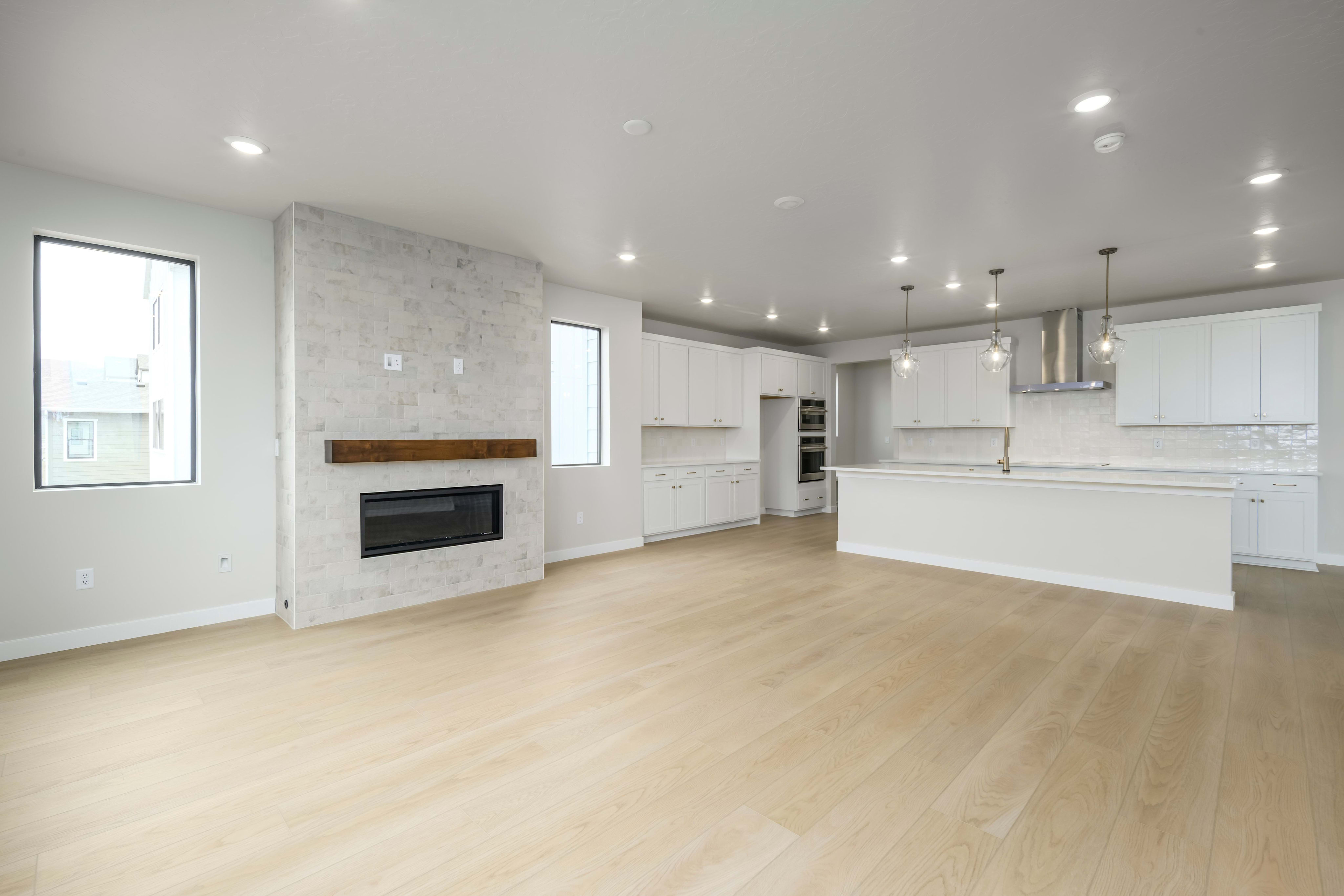 A spacious, modern kitchen with white cabinets, hardwood floors, and a fireplace in the background.