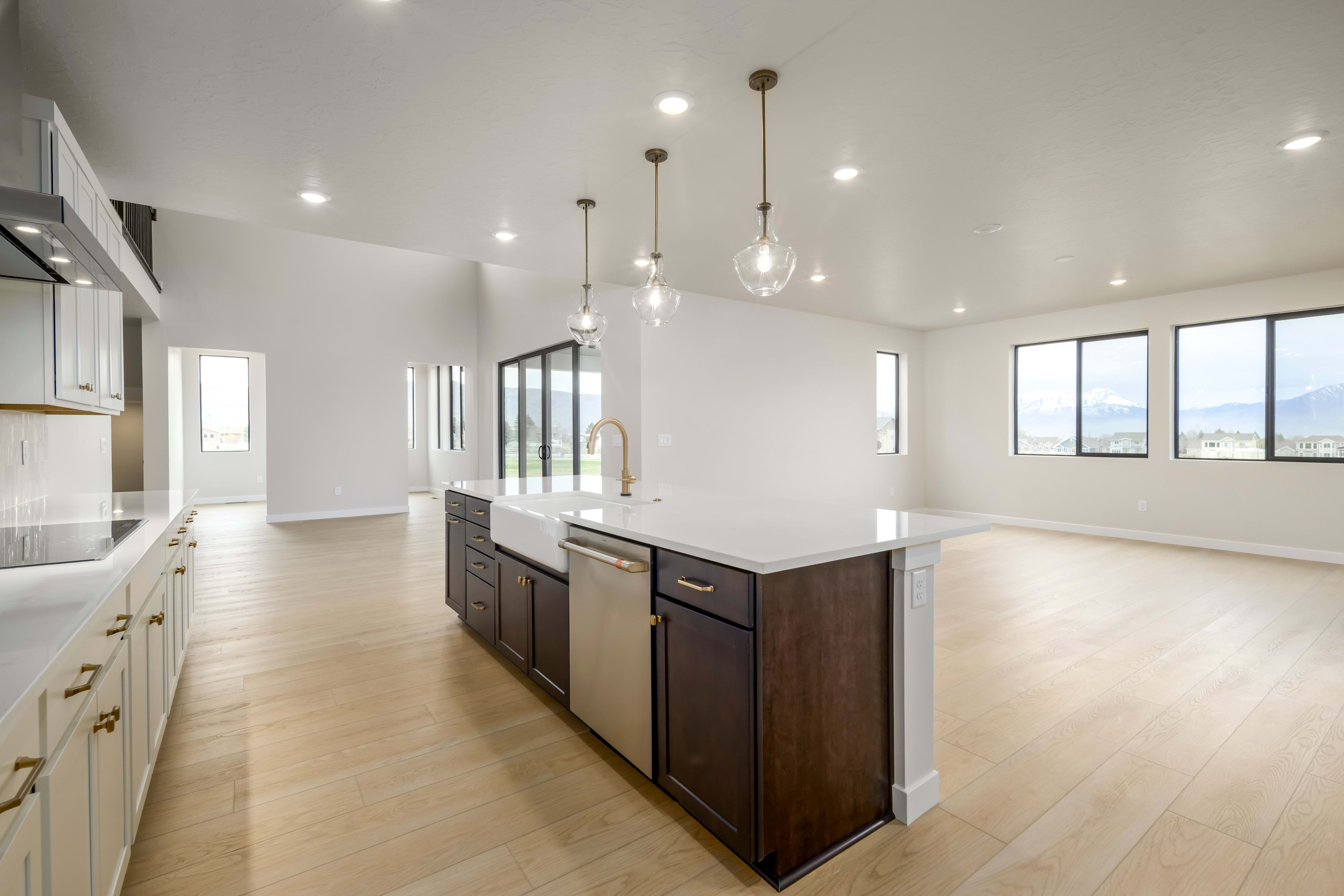 A modern, open-concept kitchen with white cabinets, dark wood accents, and pendant lighting fixtures illuminating the spacious room.