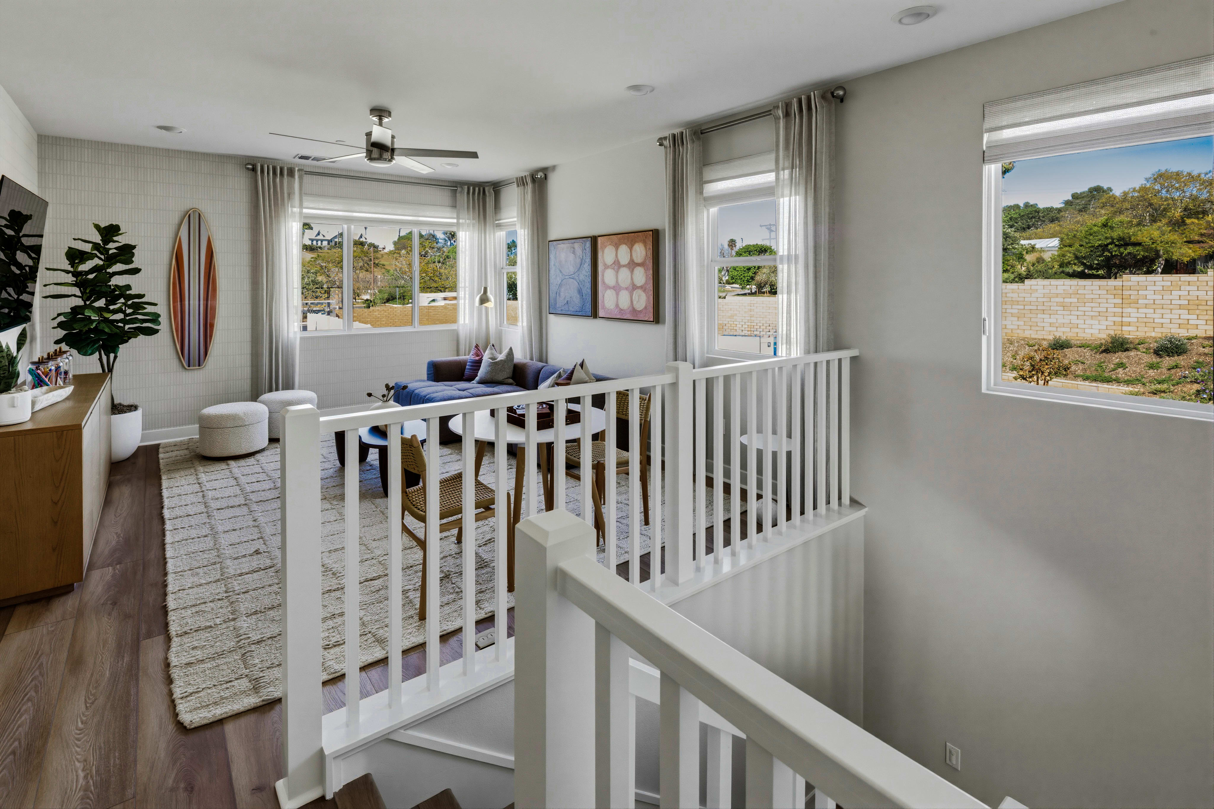 A cozy and bright nursery with a white crib and railing, surrounded by large windows overlooking a lush outdoor landscape.
