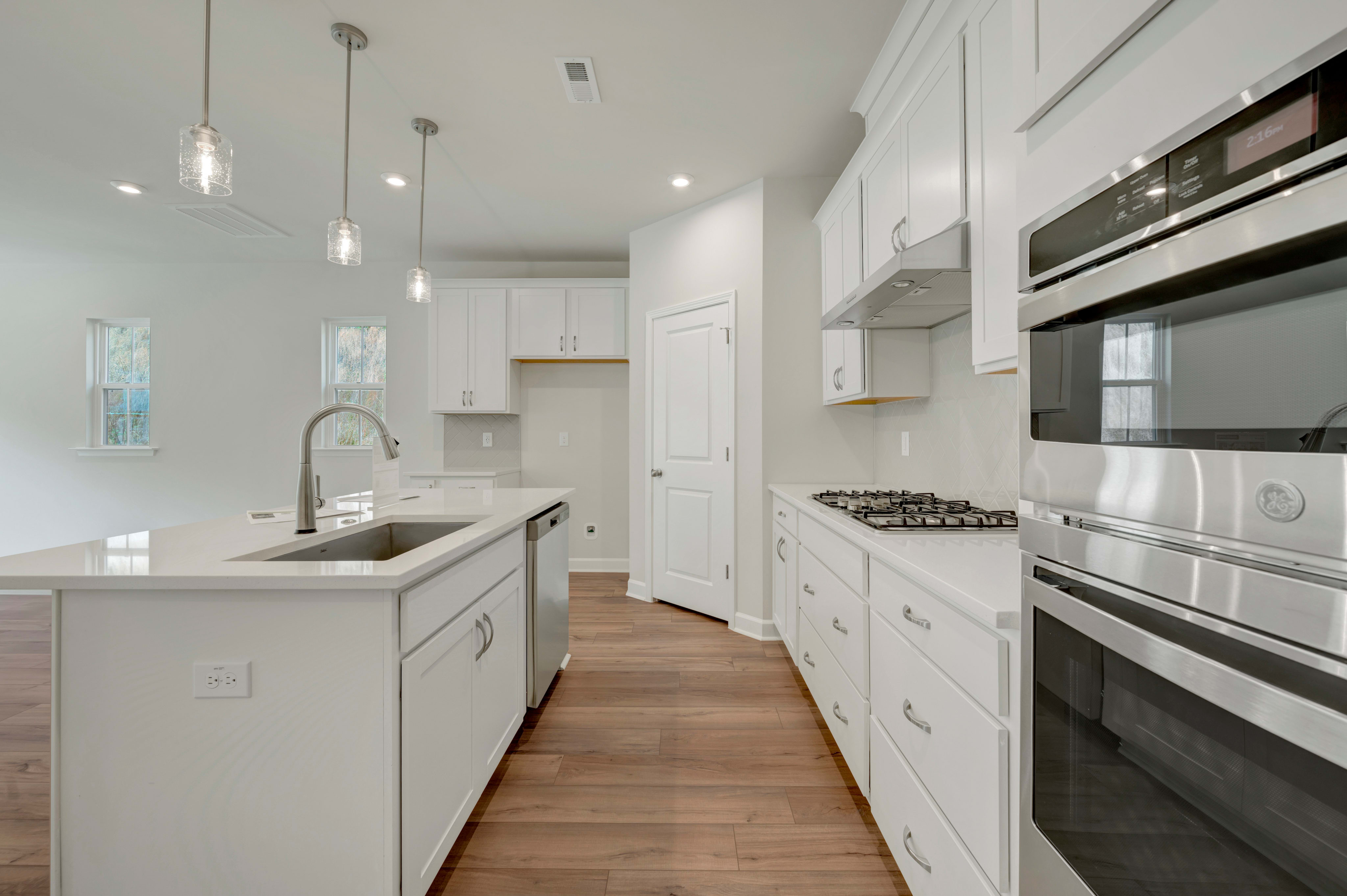 A modern, bright kitchen with white cabinets, stainless steel appliances, and a wooden floor.
