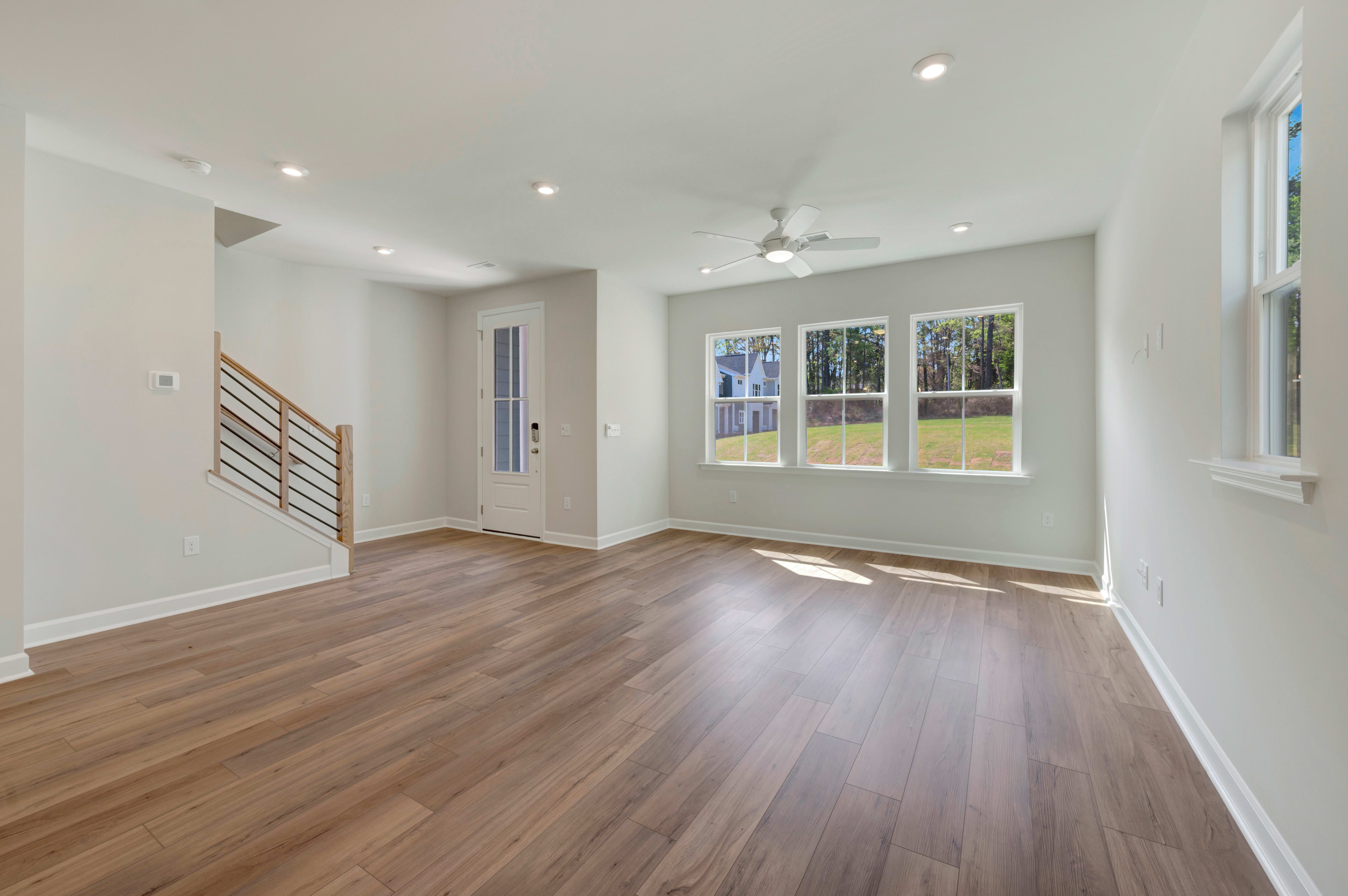 A spacious, well-lit room with hardwood floors, white walls, and large windows overlooking a scenic outdoor area.