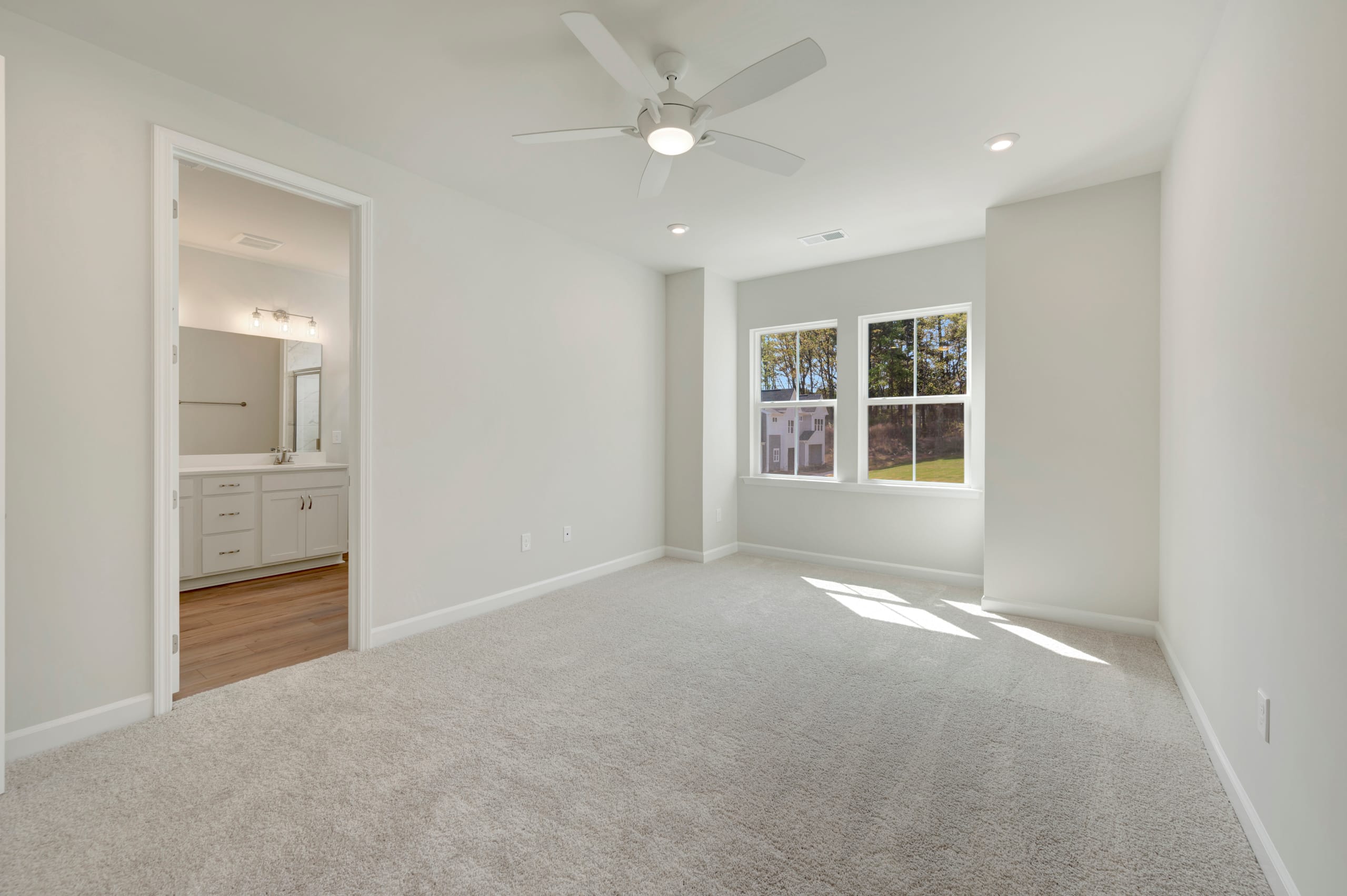 A bright and spacious room with a ceiling fan, hardwood floors, and a large window overlooking a scenic outdoor view.